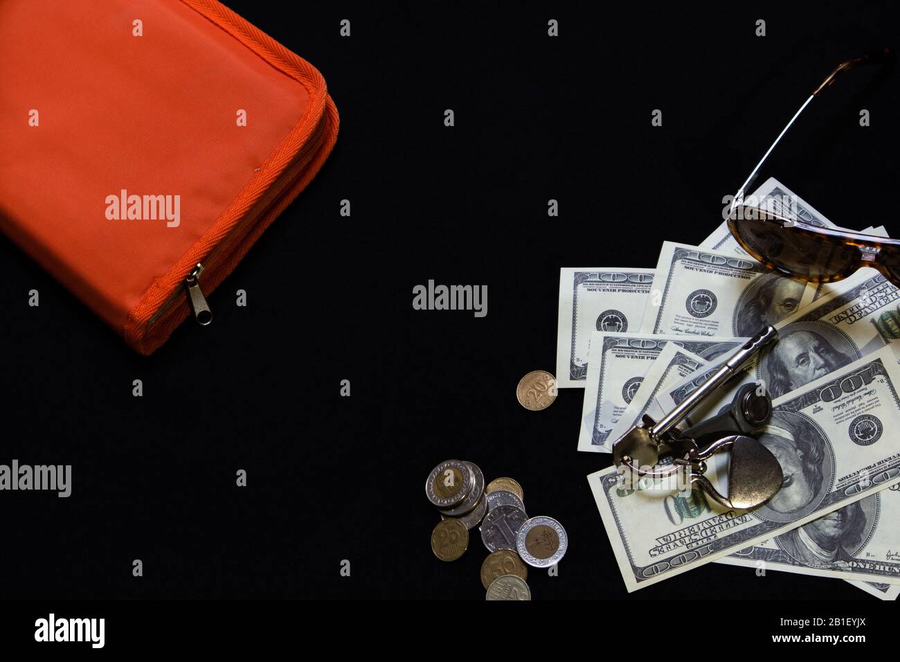 Still life with scattered hundred dollar banknotes, home keys, different coins, sunglasses and orange document case on black background Stock Photo