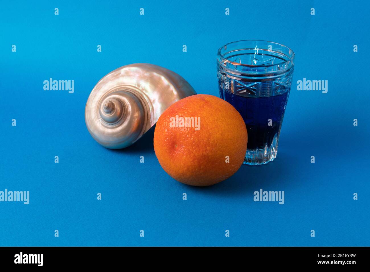 Still life with big beautiful pearl shell, bright orange and glass with blue liquid Stock Photo