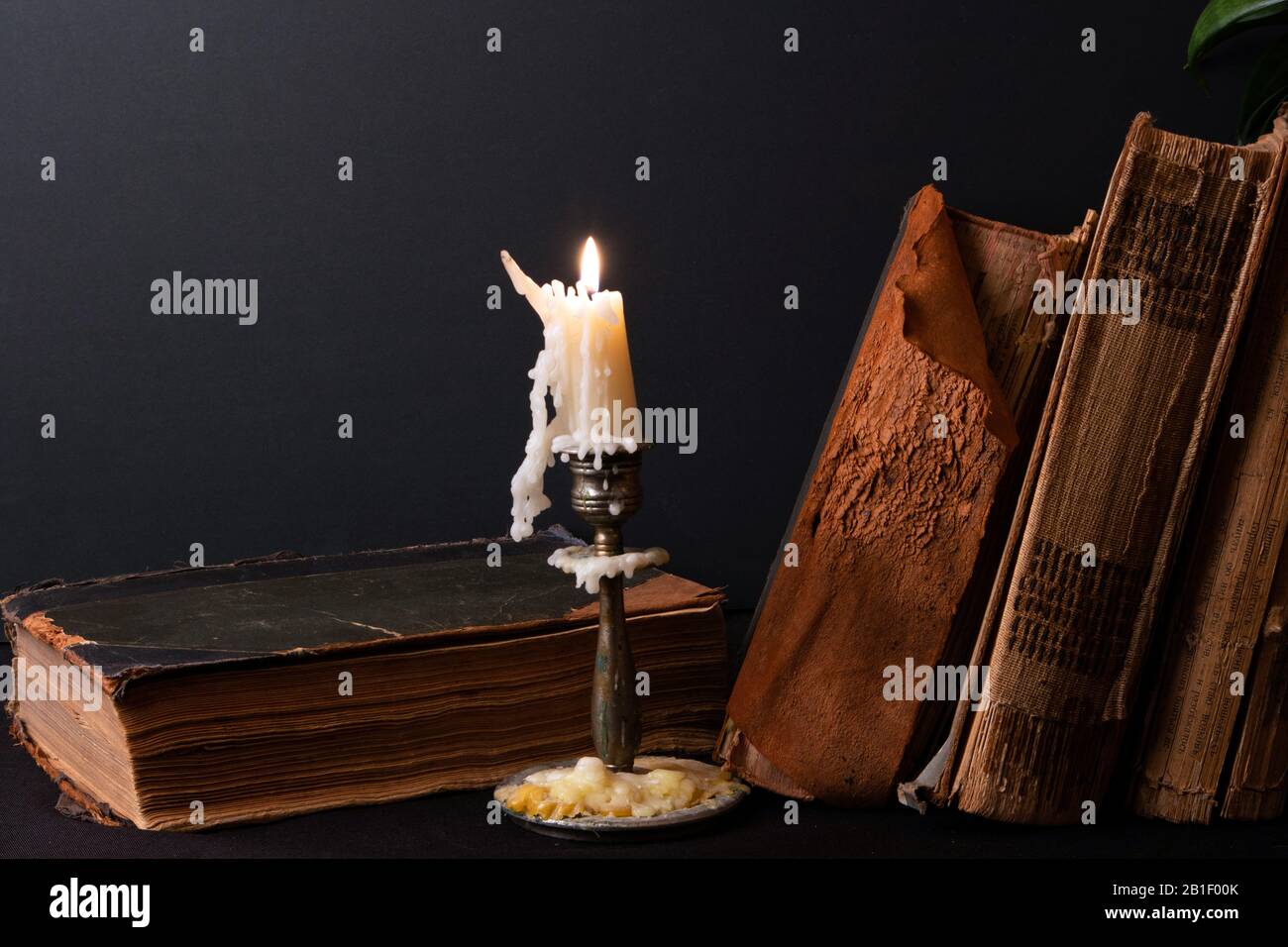 Stack of ancient books with yellowed shabby pages and candlestick with lighted candle Stock Photo