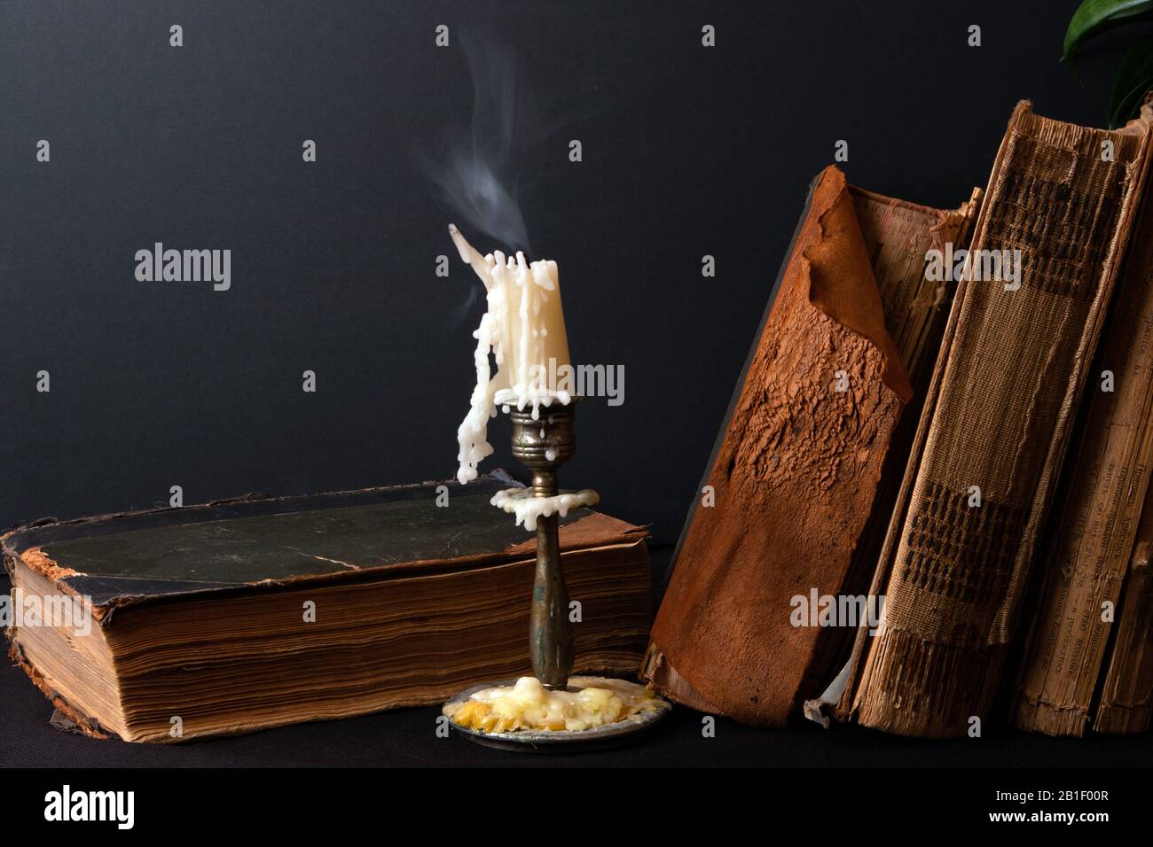 Stack of ancient books with yellowed shabby pages and candlestick with steaming candle Stock Photo