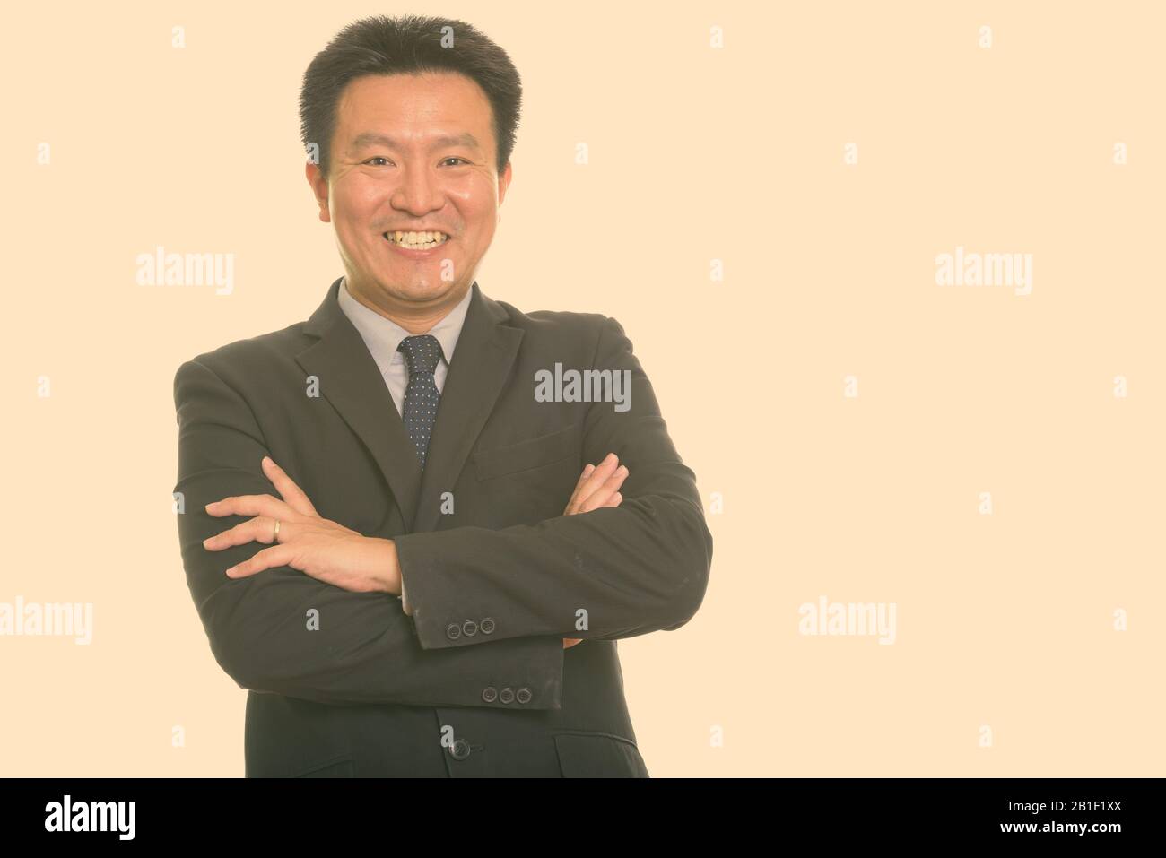 Studio shot of happy Japanese businessman smiling with arms crossed ...