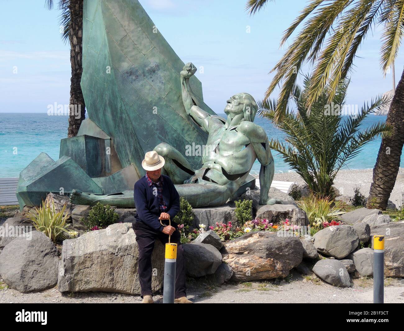 DAYDREAMING OF FORMER DAYS  La Heradurra, Almuñécar, Granada Province, Spain 2017 -  An old man reflects on former times near the statue which commemorates the  sinking offshore of 25 of the 28 galleys from the Spanish Armada . Around  5000 people lost their lives in a single day. The statue also serves as a monument to all those who go have lost their lives at  sea.. Stock Photo