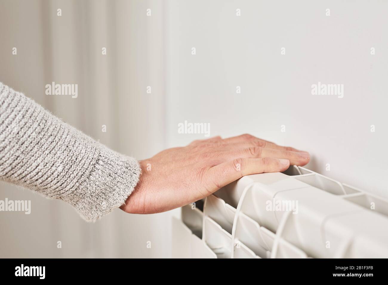 closeup of a caucasian man, wearing a pale gray sweater, touching a hot-water radiator to check its temperature or to warm his hand Stock Photo