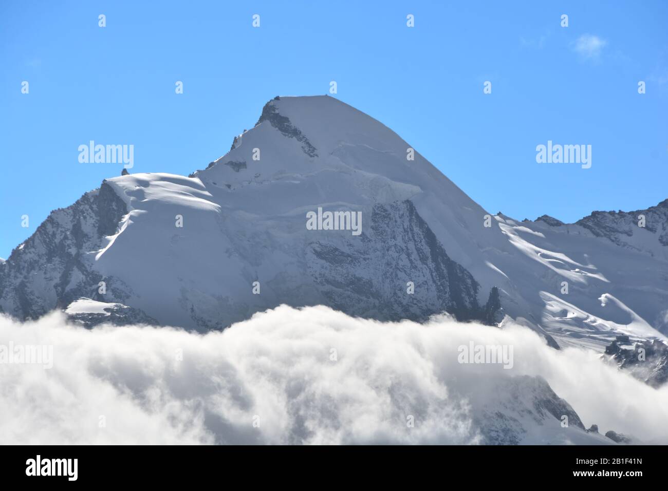 The summit of the Allalinhorn rising above the clouds. to the right the revolving glacier restaurant of Mittel Allalin above Saas Fee in the Swiss Alp Stock Photo