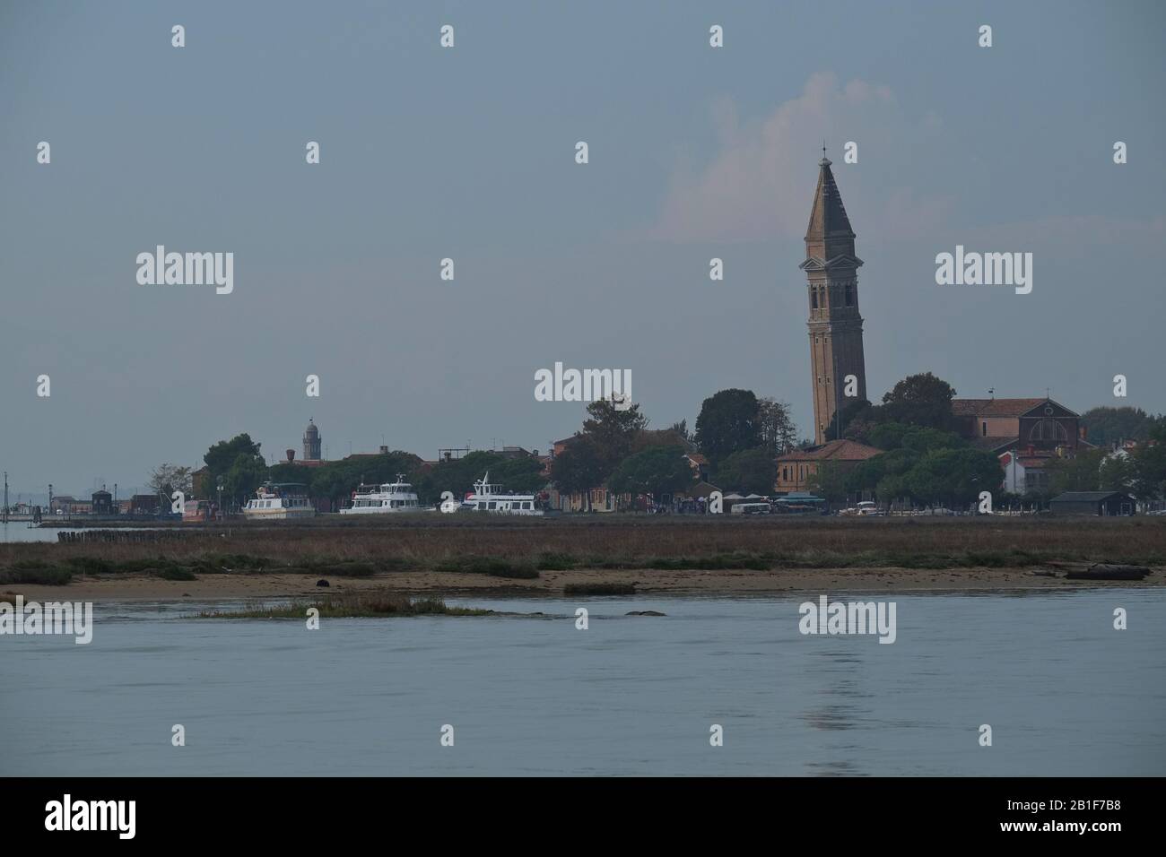 Burano Island & the ancient Chiesa di San Martino,  its leaning 17th-century church bell tower seen from the lagoon across salt marshes, Venice, Italy Stock Photo