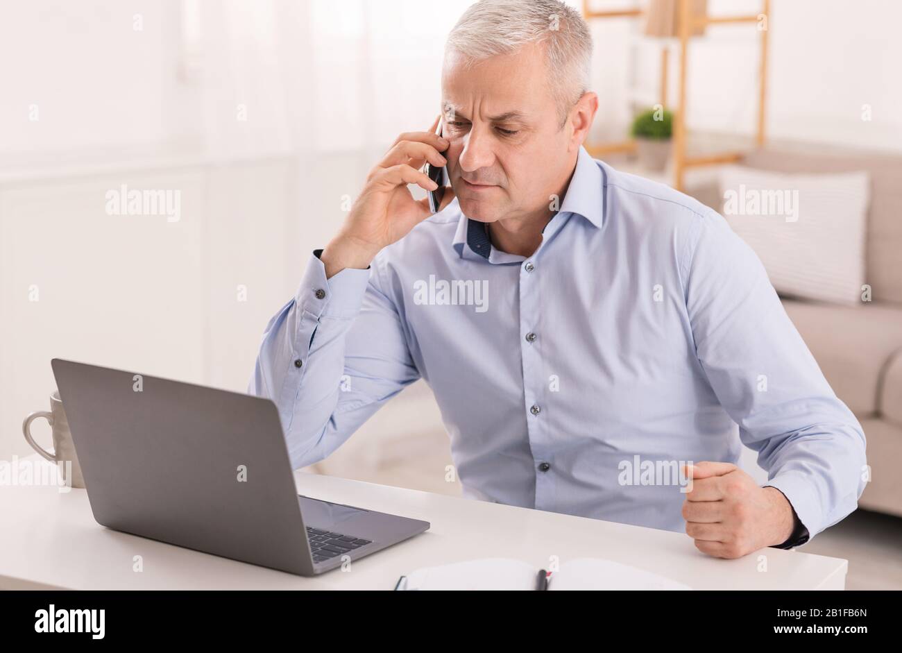 Serious mature man talking on mobile phone at office Stock Photo