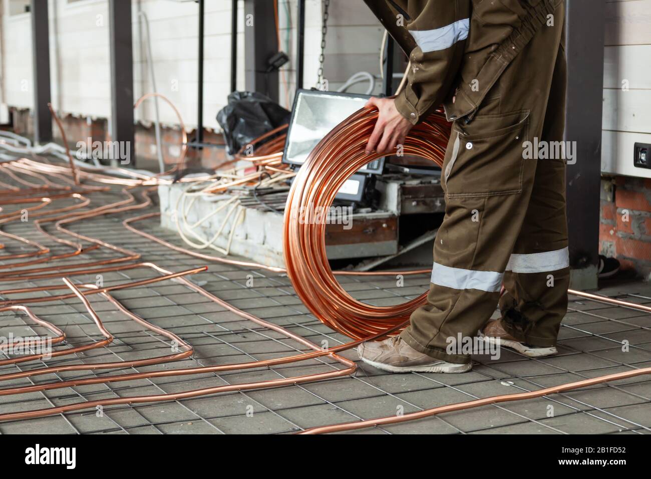 Man plumber in uniform holds large round skein of new shiny copper