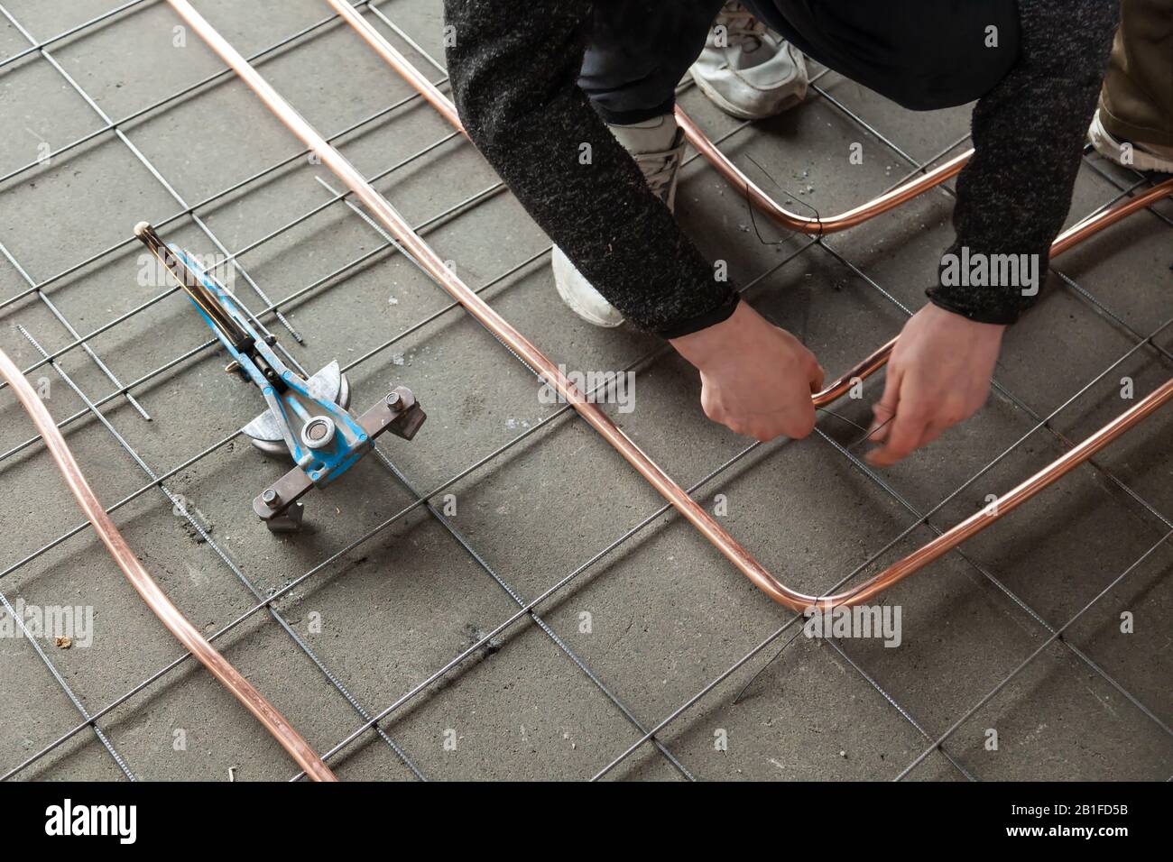 Closeup male plumber's hands bends new copper pipes by blue pipe