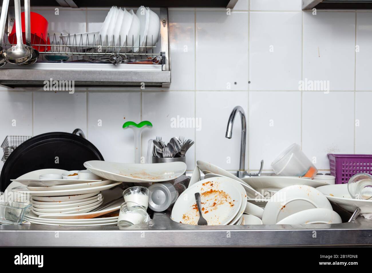 Large metal sink with dirty dishes in professional restaurant kitchen, stack of unclean white plates, crockery, appliances with leftover food, water t Stock Photo