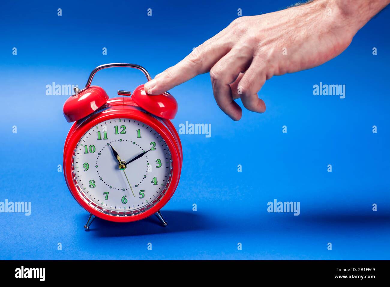 Red alarm clock on the color background. A hand of person switching off