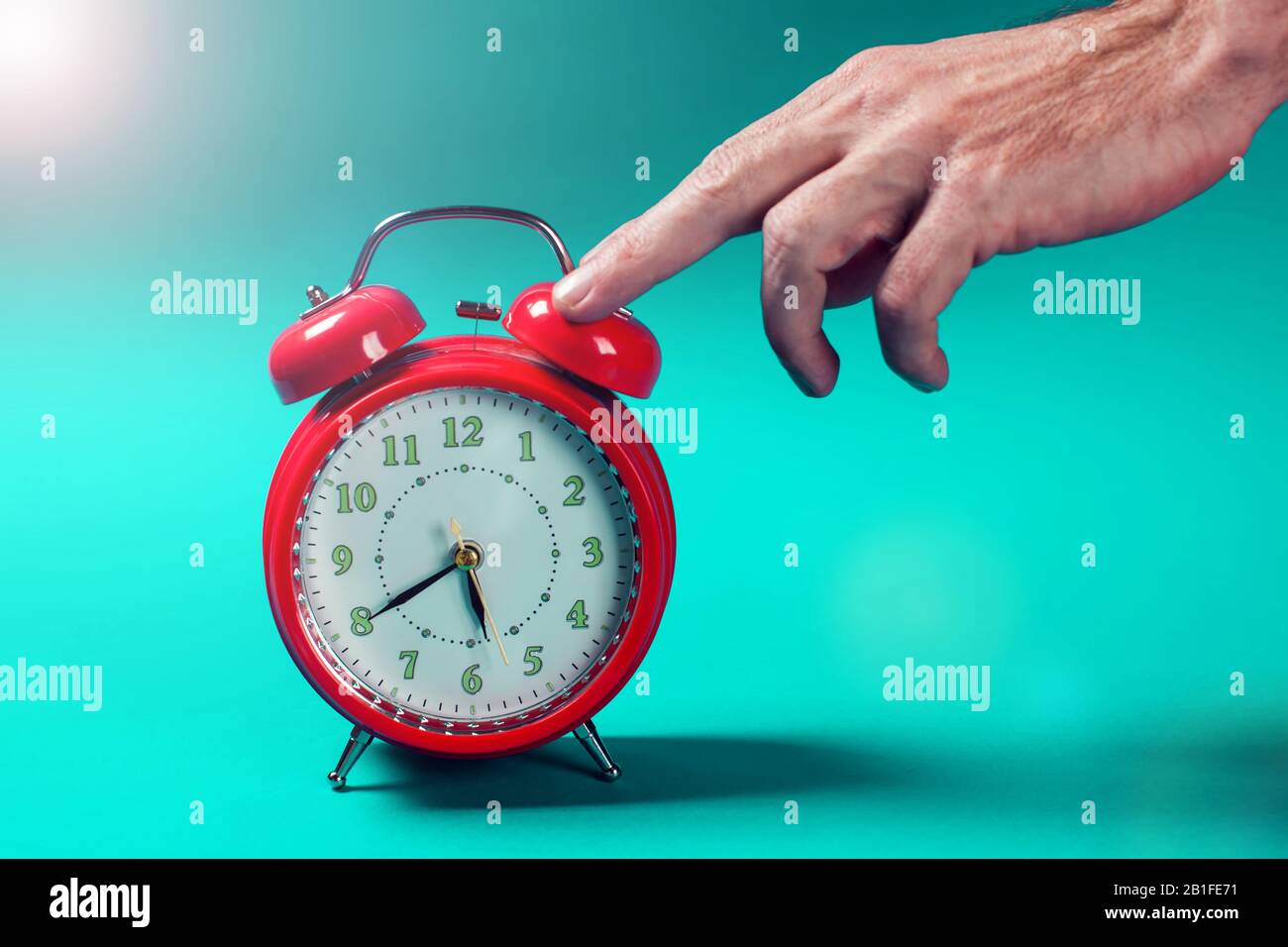 Red alarm clock on the color background. A hand of person switching off