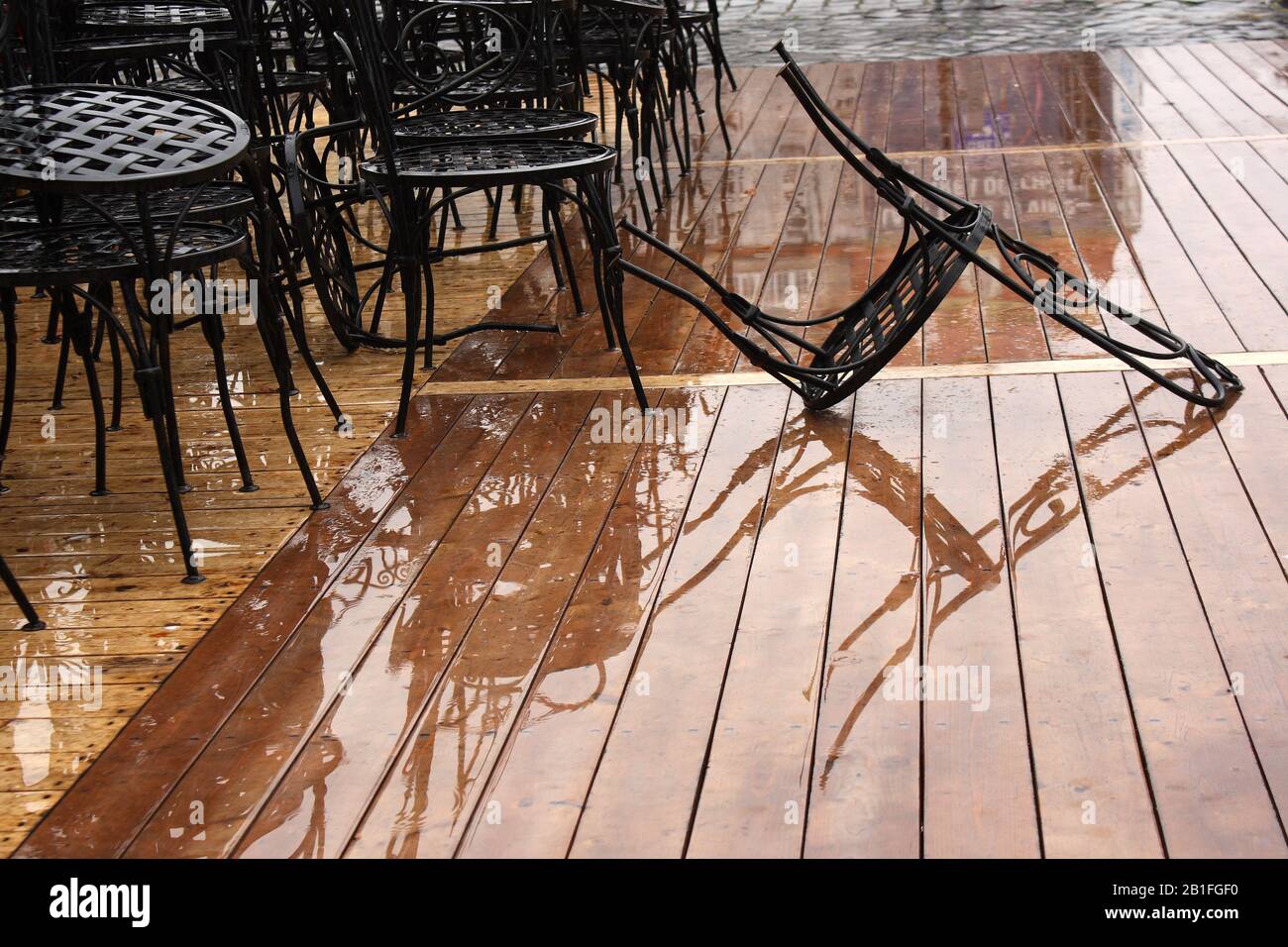Restaurant furniture in the rain. Chairs on wet wooden floor. Urban scene on wet background