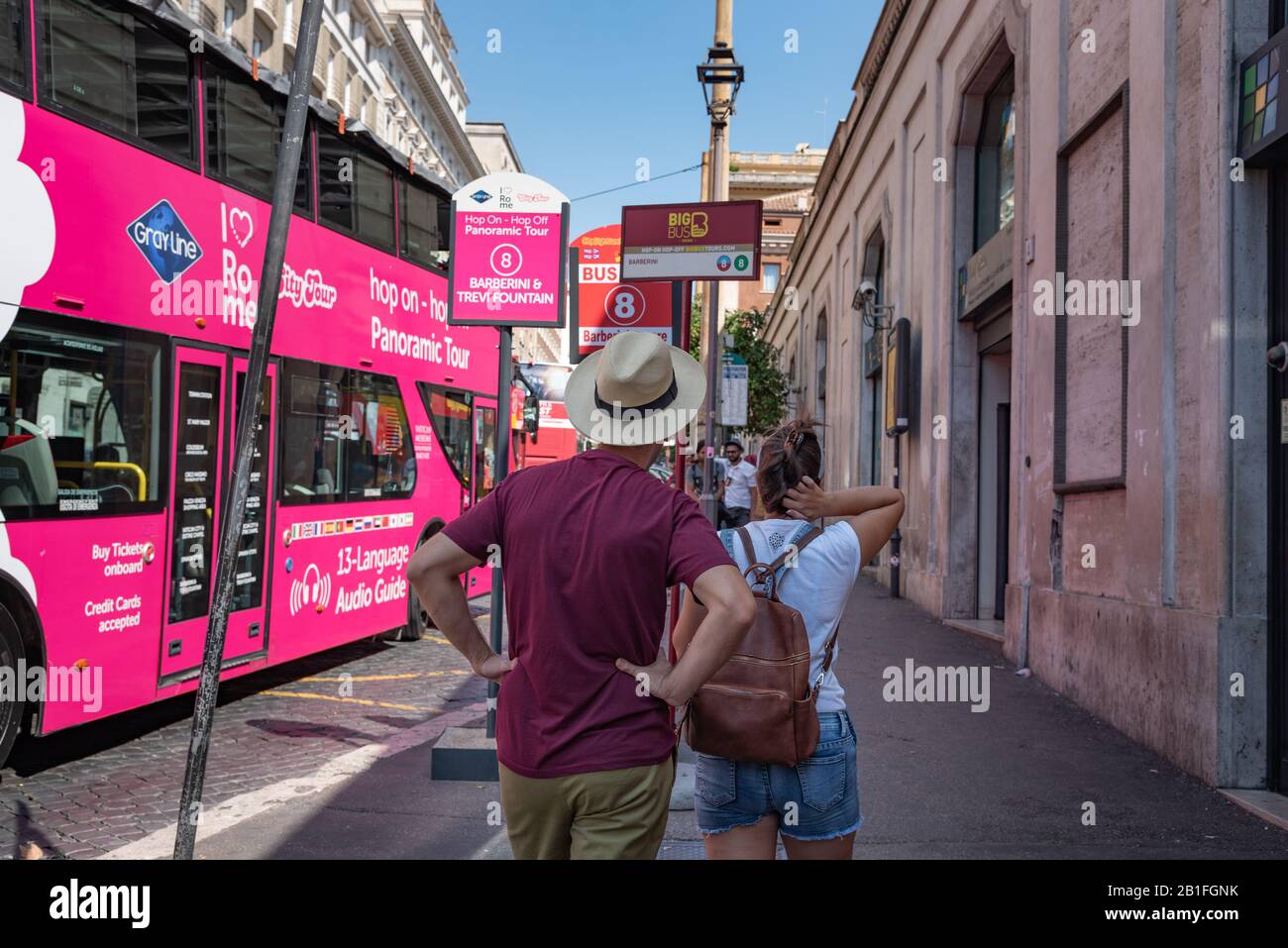 Rome, Italy - September 5, 2019: Couple of tourists waiting for a bus on bus station via Piazza Barberini. Two floor pink bus on background. Stock Photo