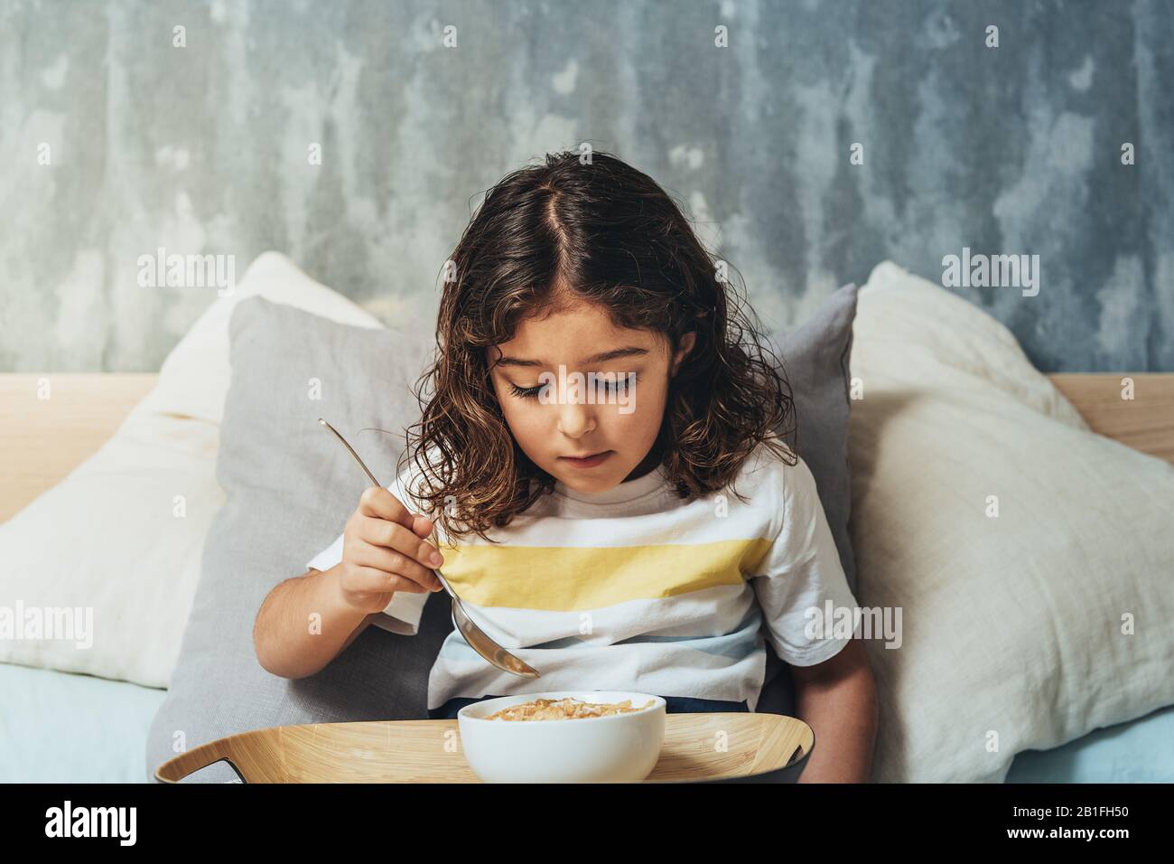 little girl having sunday breakfast in her parents' bed. Child enjoying a bowl of cereals at home in the morning, concept of healthy lifestyle and foo Stock Photo
