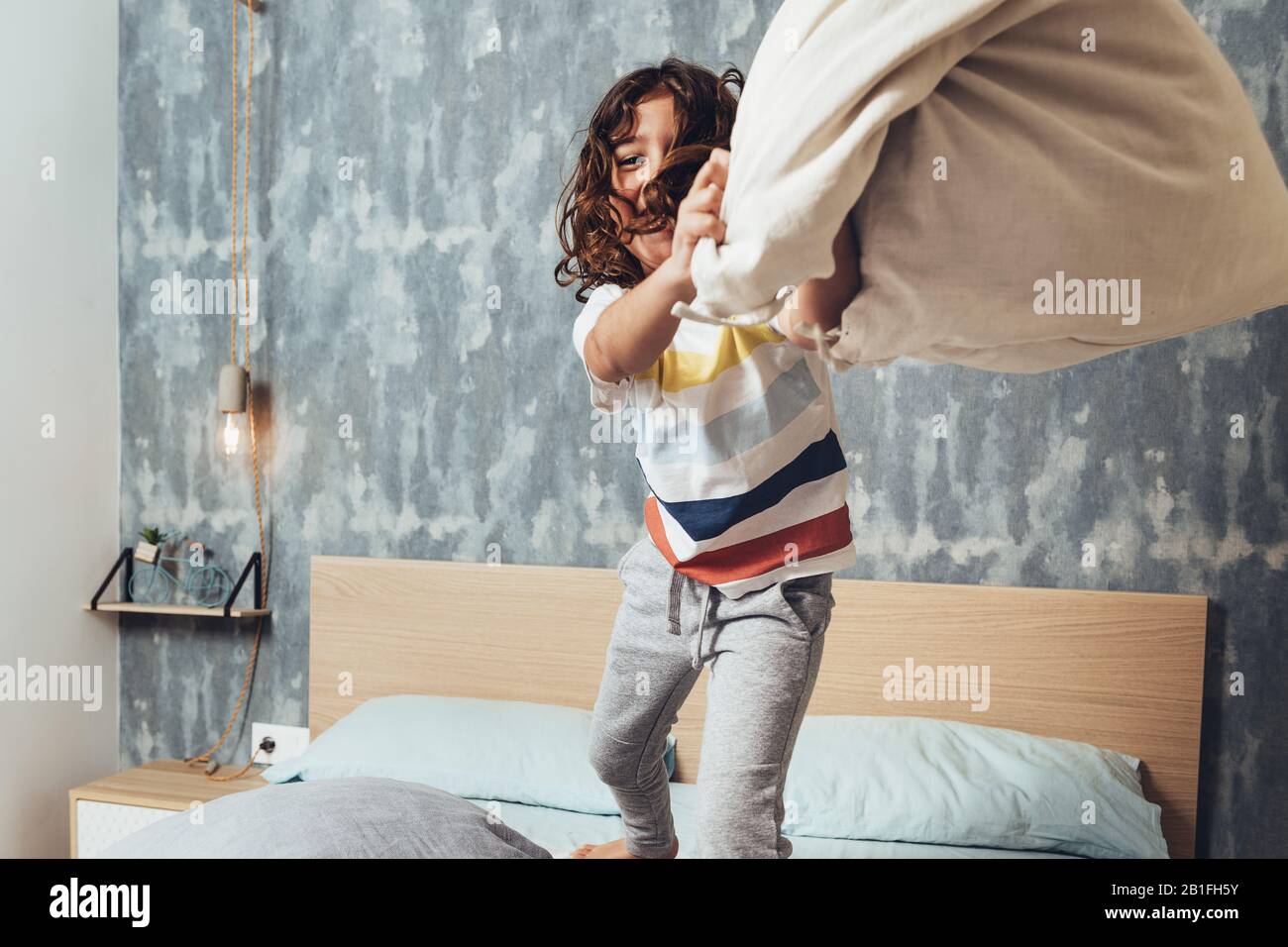 funny little girl throwing a cushion standing on her parents bed, home