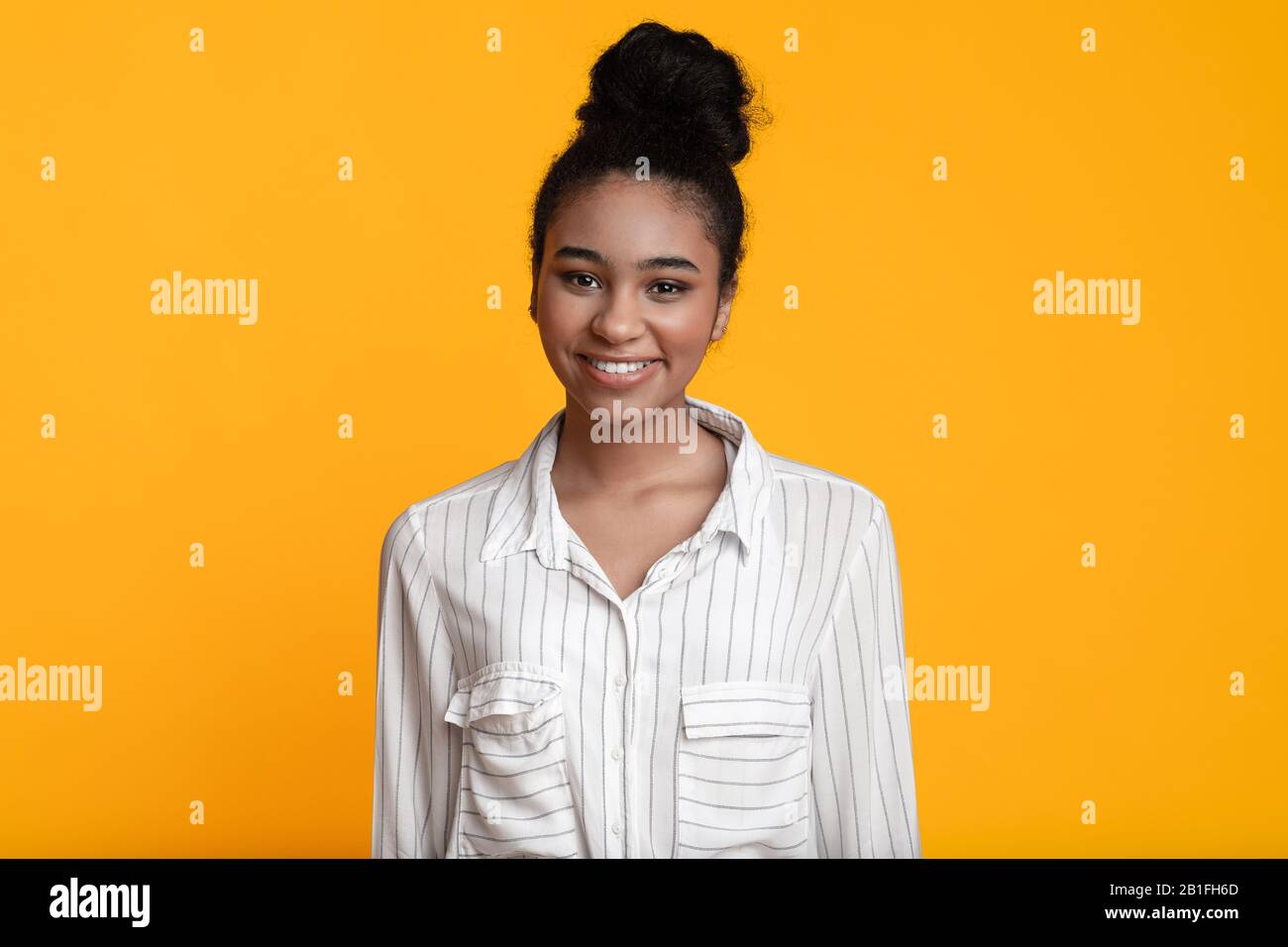 Portrait Of Smiling Afro Woman With Bun Hairstyle Over Yellow Background Stock Photo