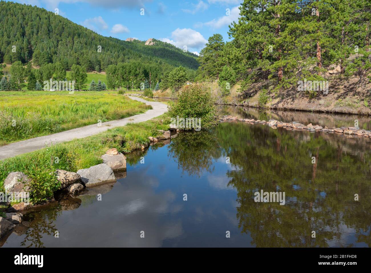 Landscape of pond, walking path and forested hills at Dedisse Park in Evergreen, Colorado Stock Photo