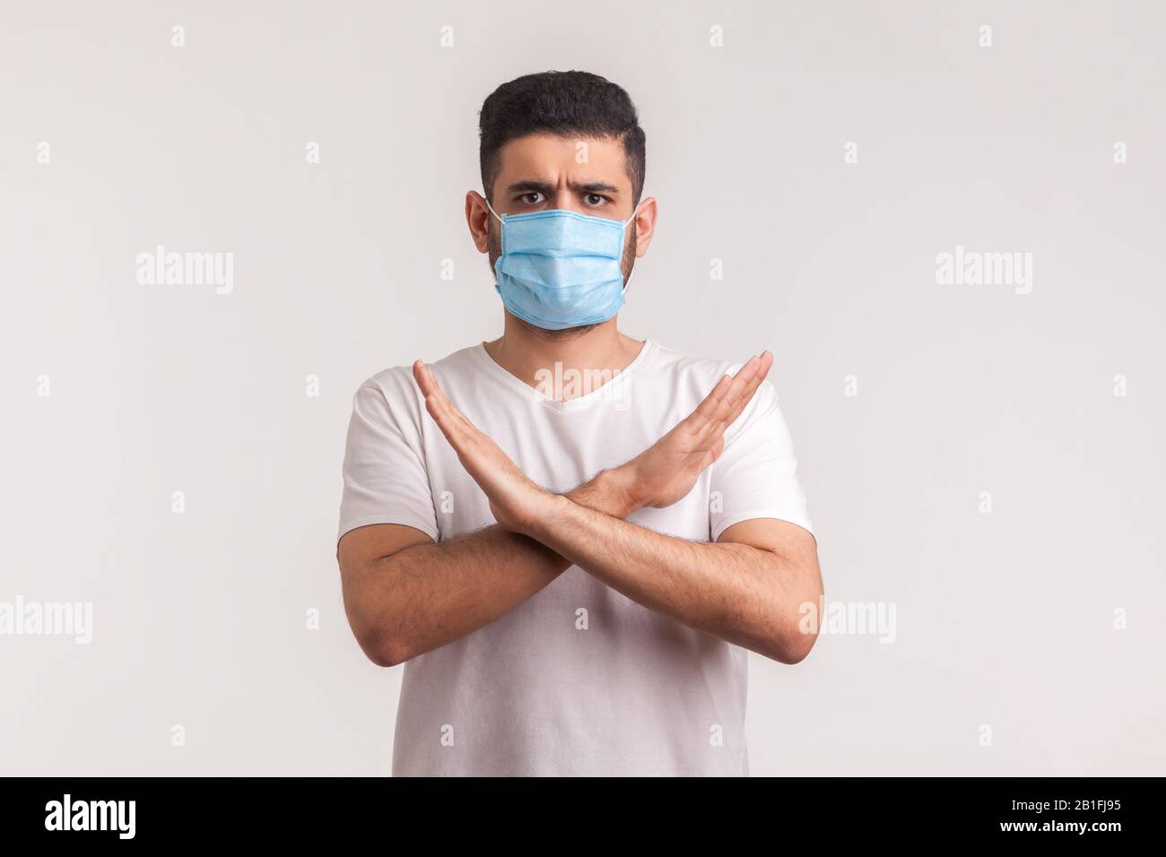 Man in protective hygienic mask standing with crossed arms, gesturing stop, warning of coronavirus epidemic, infection, respiratory diseases such as f Stock Photo