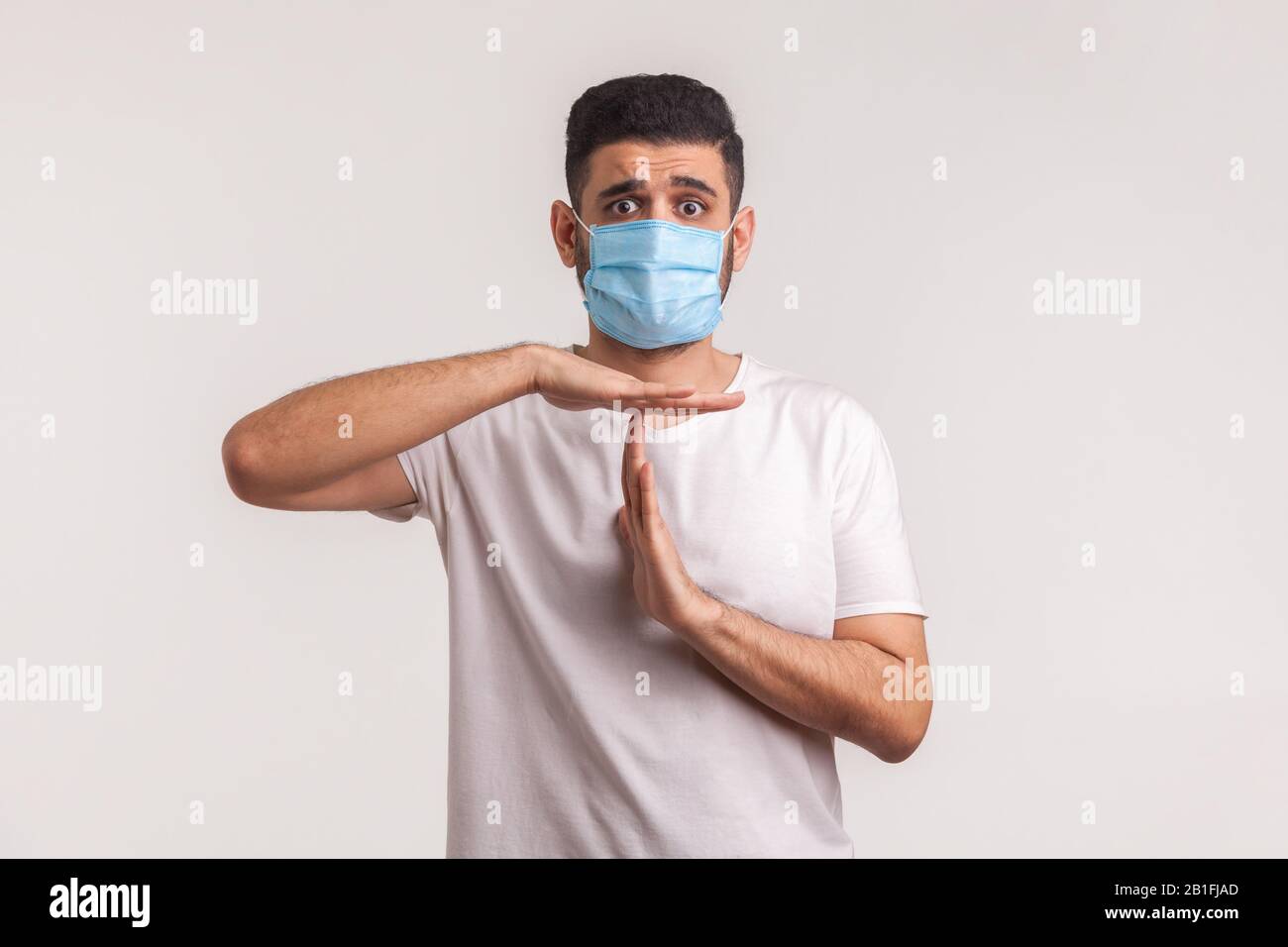 Frightened man in protective hygienic mask showing time out gesture, pleading to stop coronavirus epidemic, infection, respiratory diseases such as fl Stock Photo