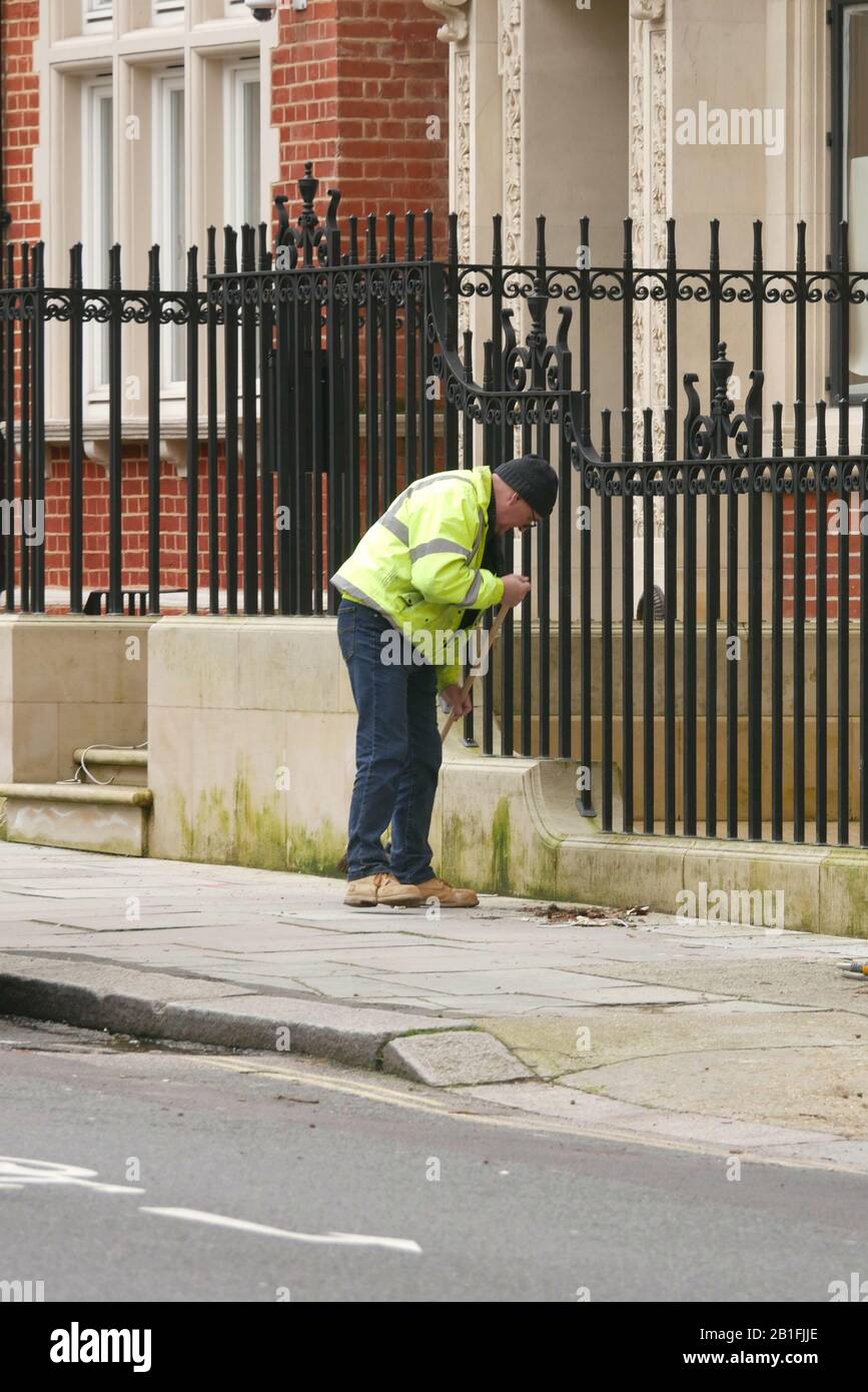 Older man sweeping the outside pavement of a block of flats Stock Photo
