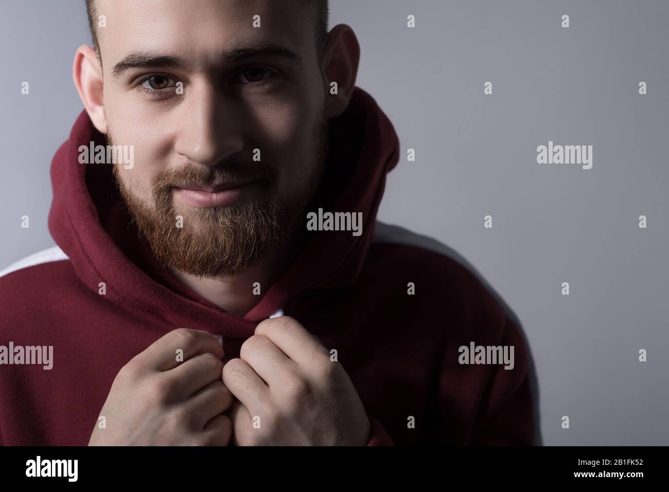 closeup, dramatic portrait of a handsome bearded guy of twenty five years old, in a red warm sweater with a hood, holding hands, tightening the ropes. Stock Photo