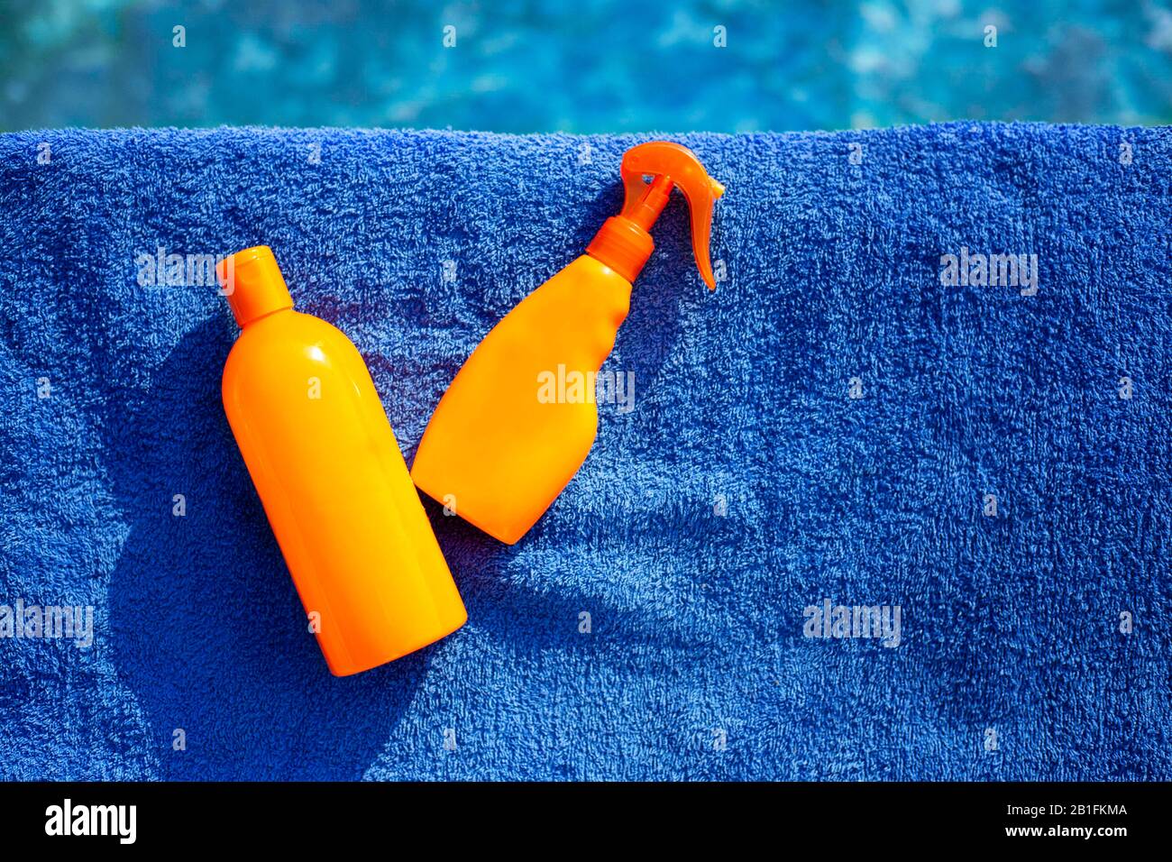 Cosmetic sunscreen products, set different orange bottles of sun protection body cream on blue towel against swimming pool. Skin care and protection Stock Photo