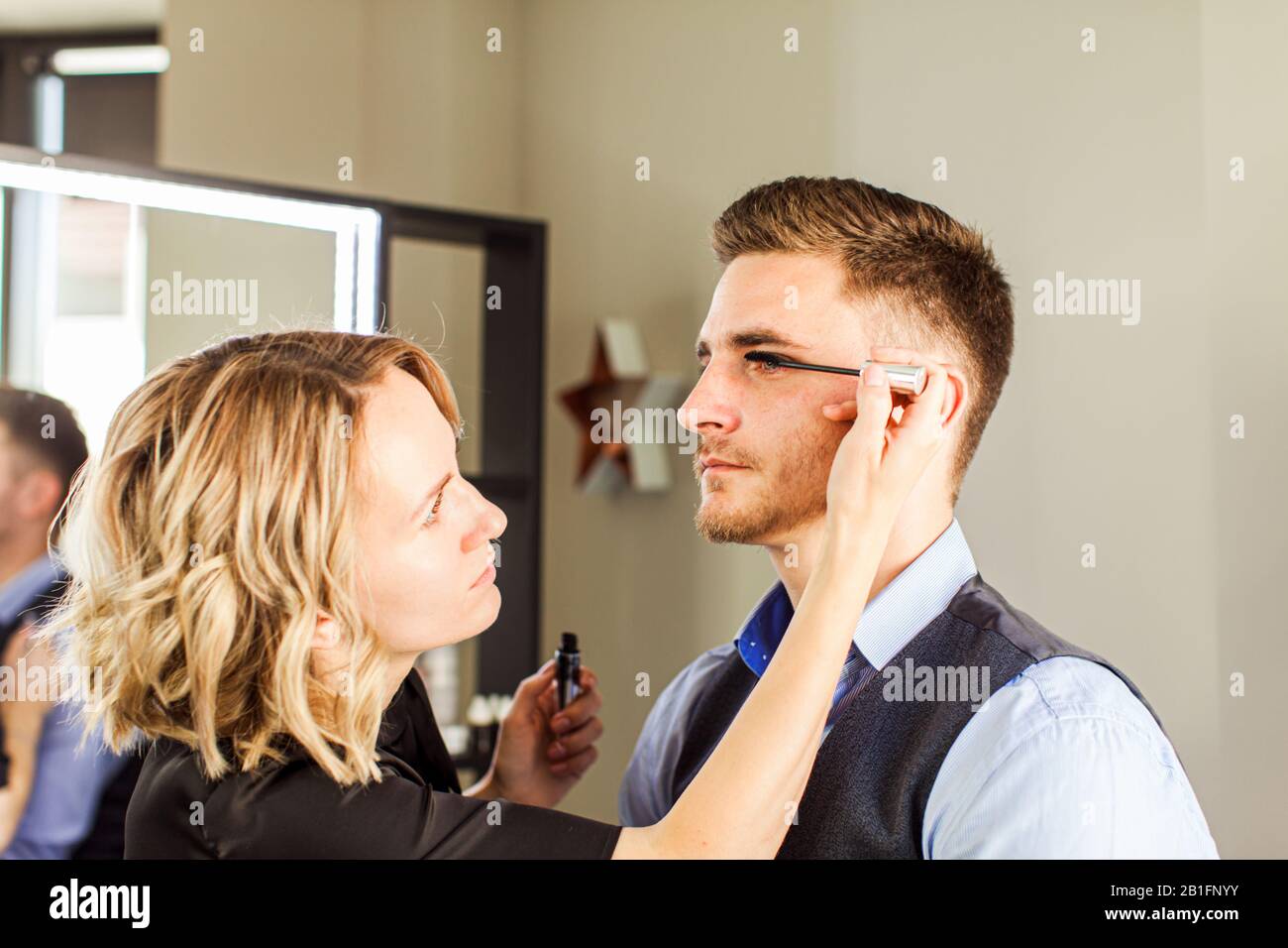 Professional actor preparation before shoot. Handsome young man applying by professional make up of visagist. Stock Photo