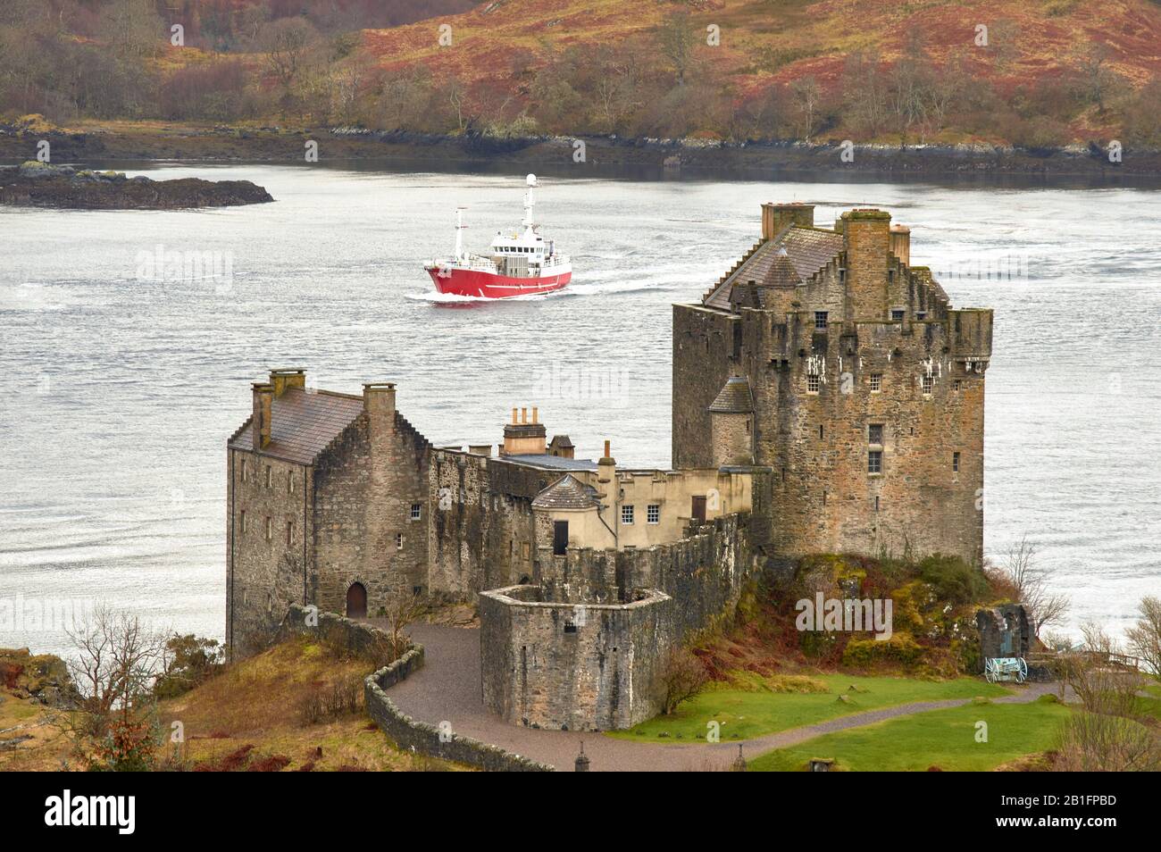 EILEAN DONAN CASTLE LOCH DUICH DORNIE SCOTLAND WINTER THE CASTLE OVERLOOKING THE WATERS OF THE LOCH WITH A RED BOAT Stock Photo