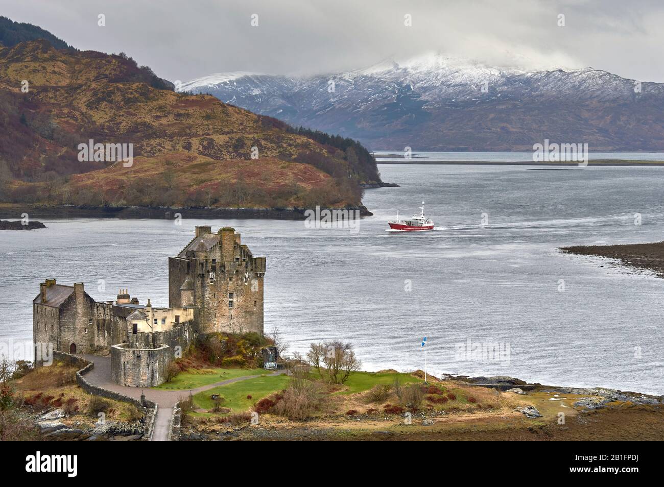 EILEAN DONAN CASTLE LOCH DUICH DORNIE SCOTLAND WINTER THE CASTLE OVERLOOKING THE WATERS OF THE LOCH WITH RED BOAT Stock Photo