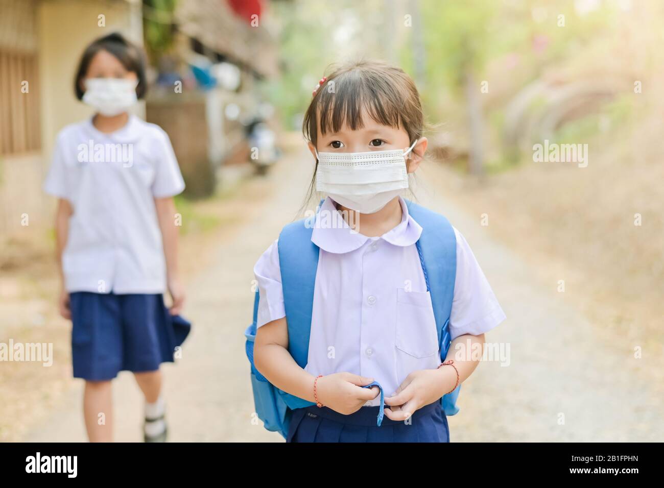 Little school girl has mask protect herself from Corona virus COVID-19 when child go to school,Student with a mask on her nose for safety outdoor Stock Photo
