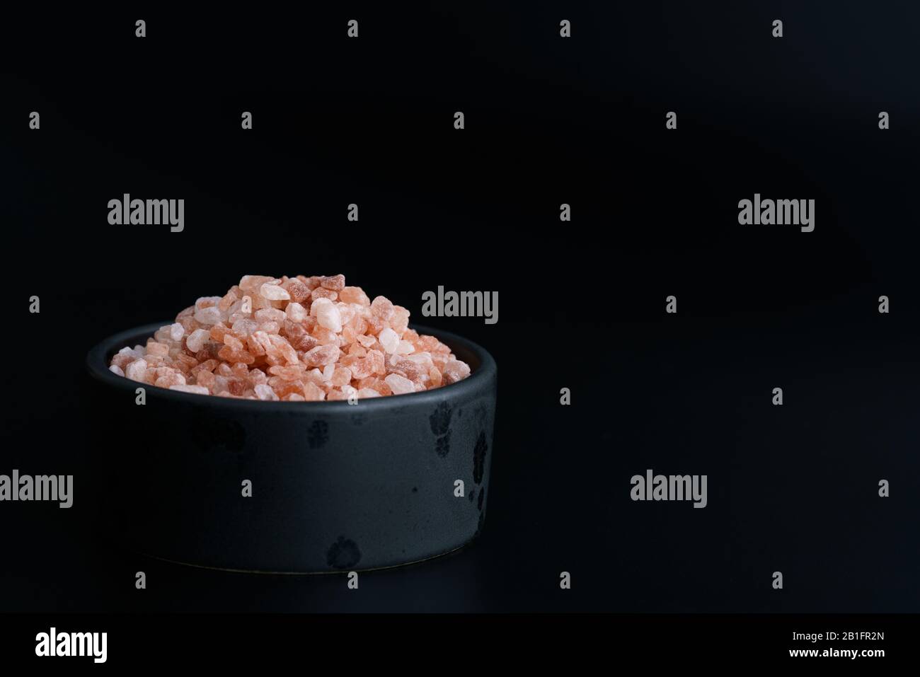 Pink Himalayan salt in black ceramic bowl. Black background, high resolution Stock Photo