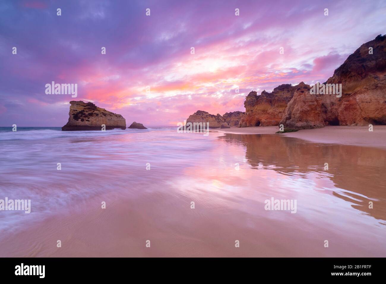 A colorful sunset reflected on the wet shores of Praia Dos Tres Irmaos. Alvor, Portimao, Algarve, Portugal,Europe. Stock Photo
