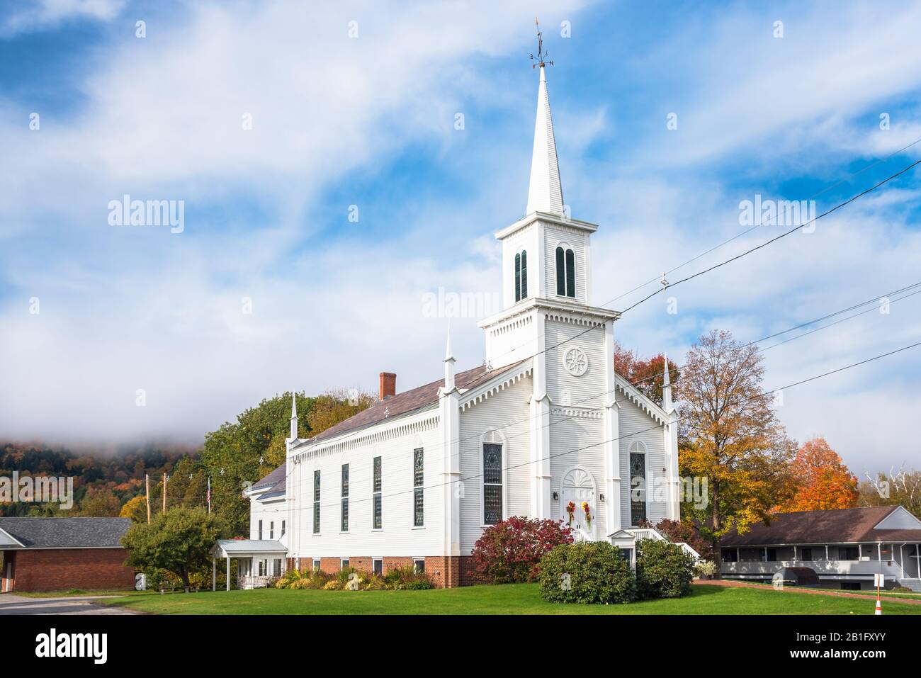 Traditional white American wooden church at the foot of a forested hill shrouded in morning fog on a autumn day Stock Photo