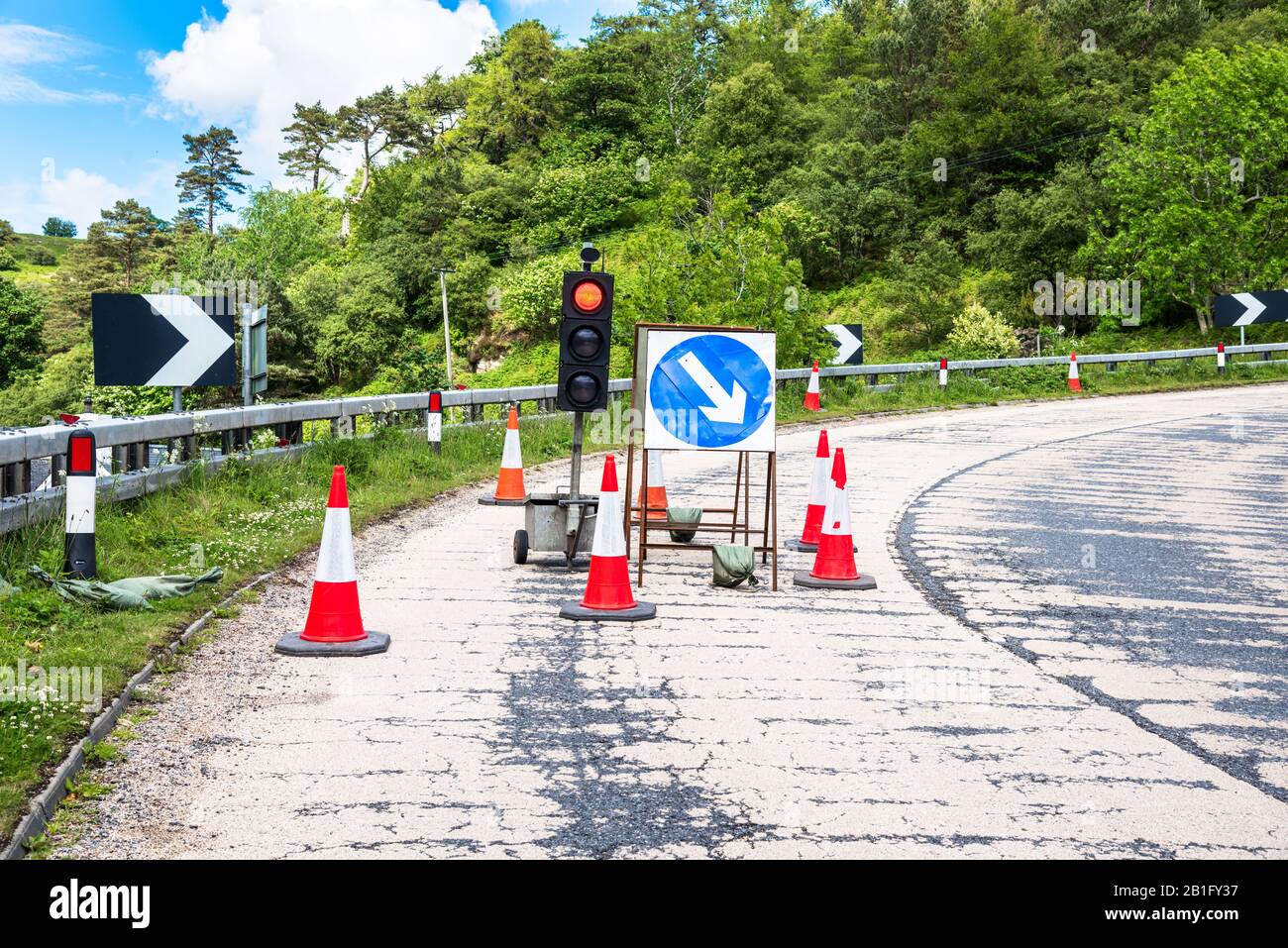 Taffic lights, sign and cones at the beginning of a roadworks area on a mountain road on a clear spring day Stock Photo