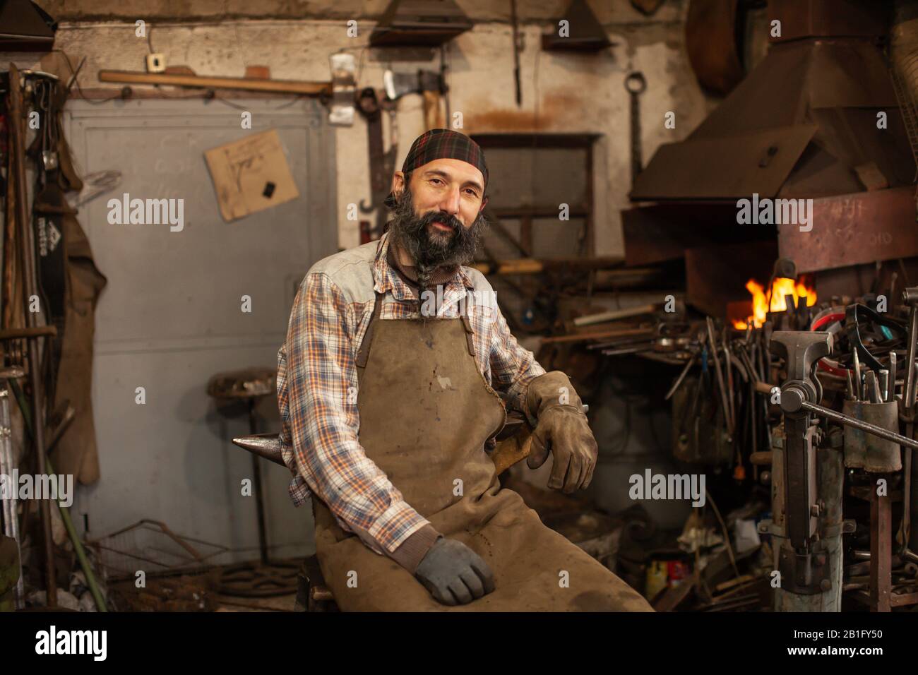 Bearded blacksmith after working in his workshop. Blacksmith's workshop. Stock Photo