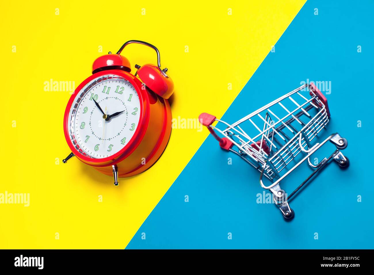 Red alarm clock, small shopping trolley on color background. Shopping concept Stock Photo