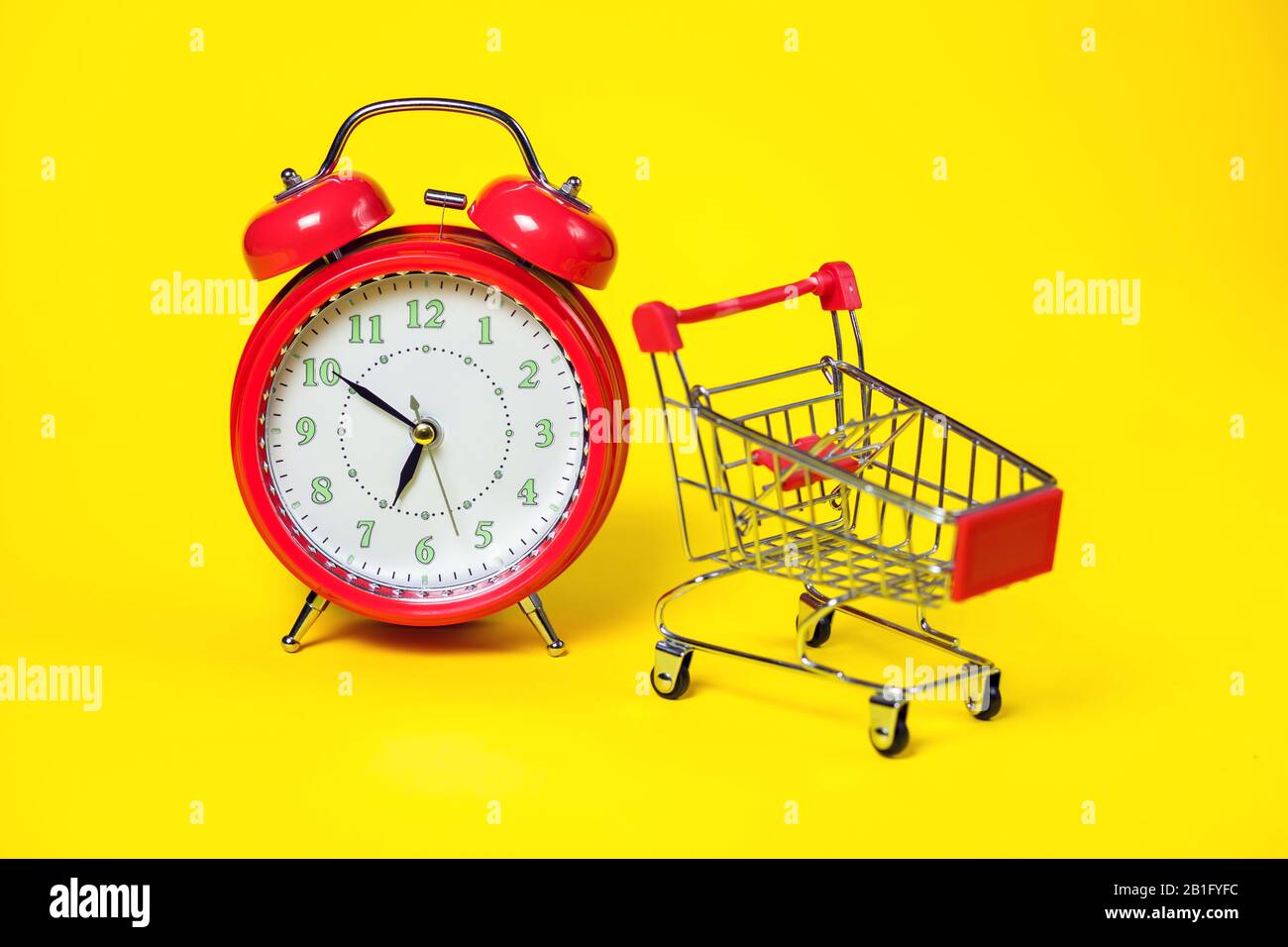 Red alarm clock, small shopping trolley on color background. Shopping concept Stock Photo