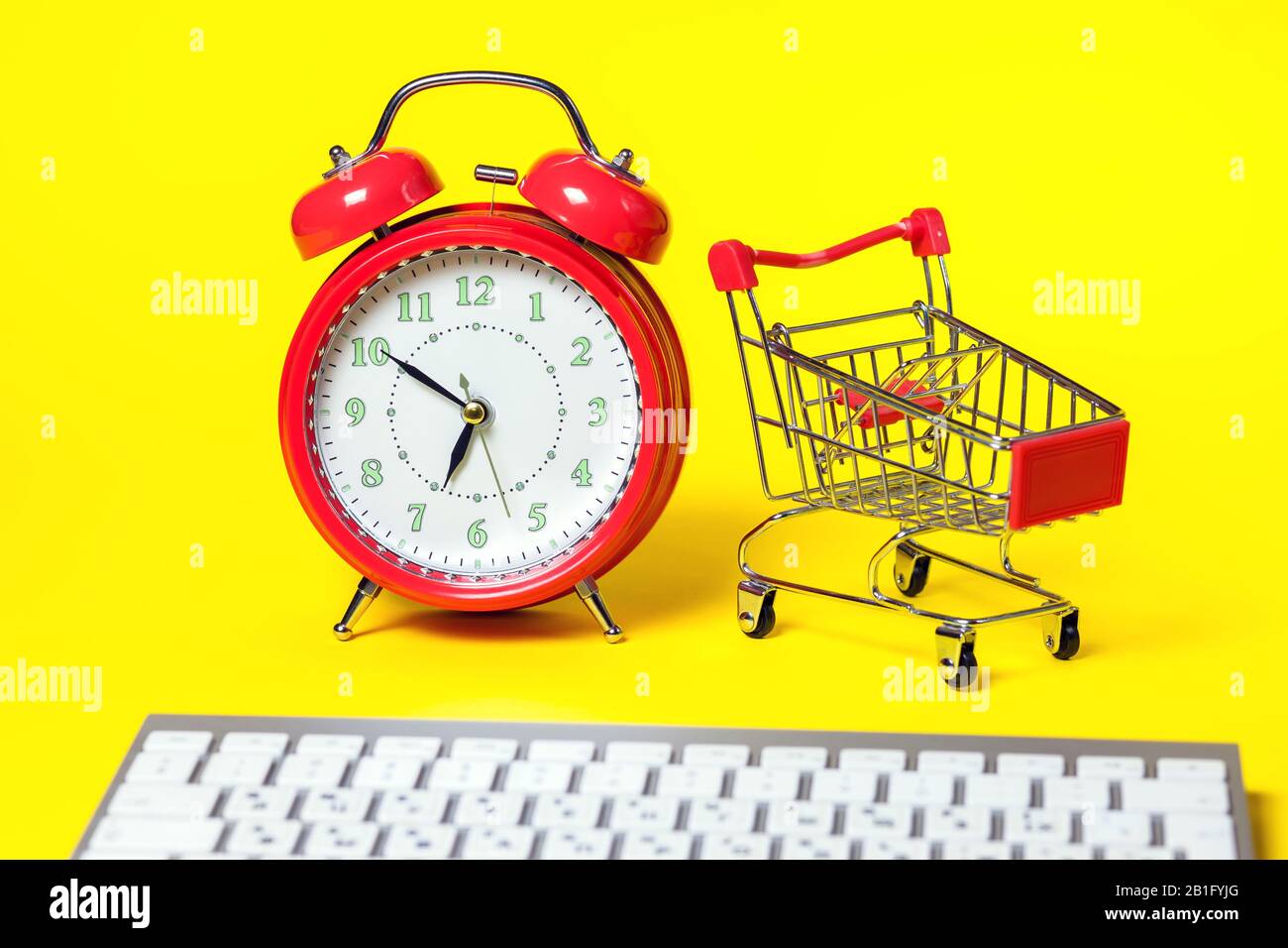 Red alarm clock, small shopping trolley, keyboard on color background