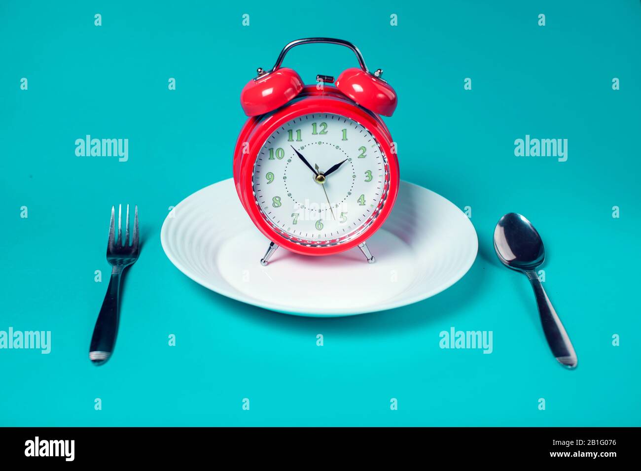 Red alarm clock on white plate on color background. Healthcare and food concept Stock Photo