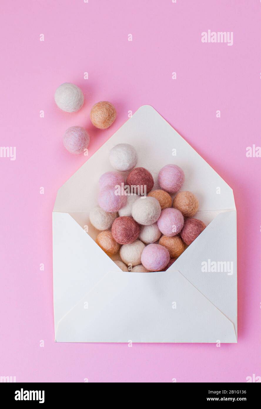 Minimal composition with felt balls flying out from opened envelope over pink background Stock Photo