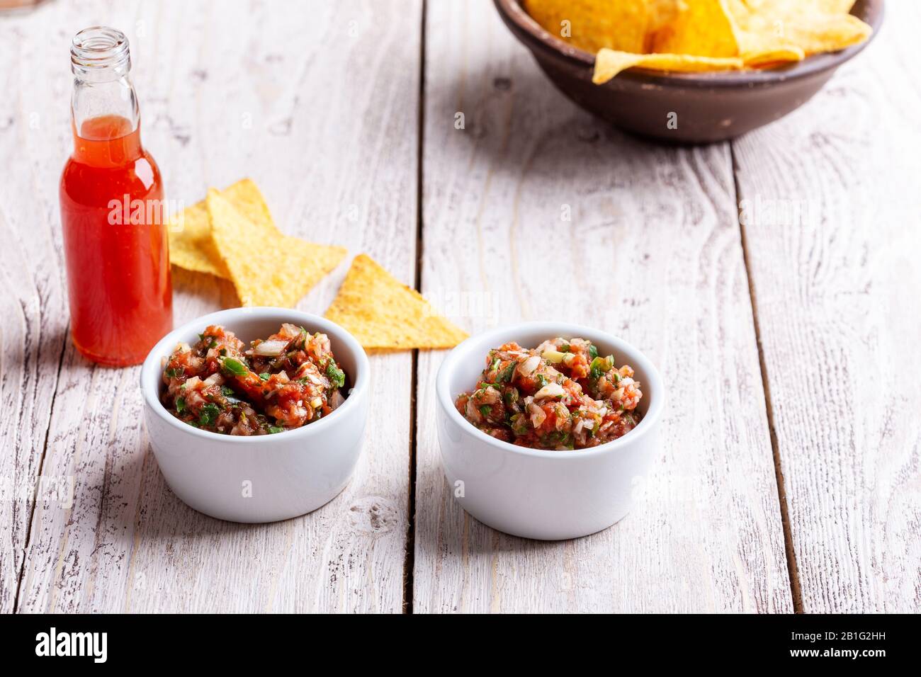 Two bowls full of salsa dip, hot red chili sauce bottle and tortilla chips on rustic wooden table Stock Photo