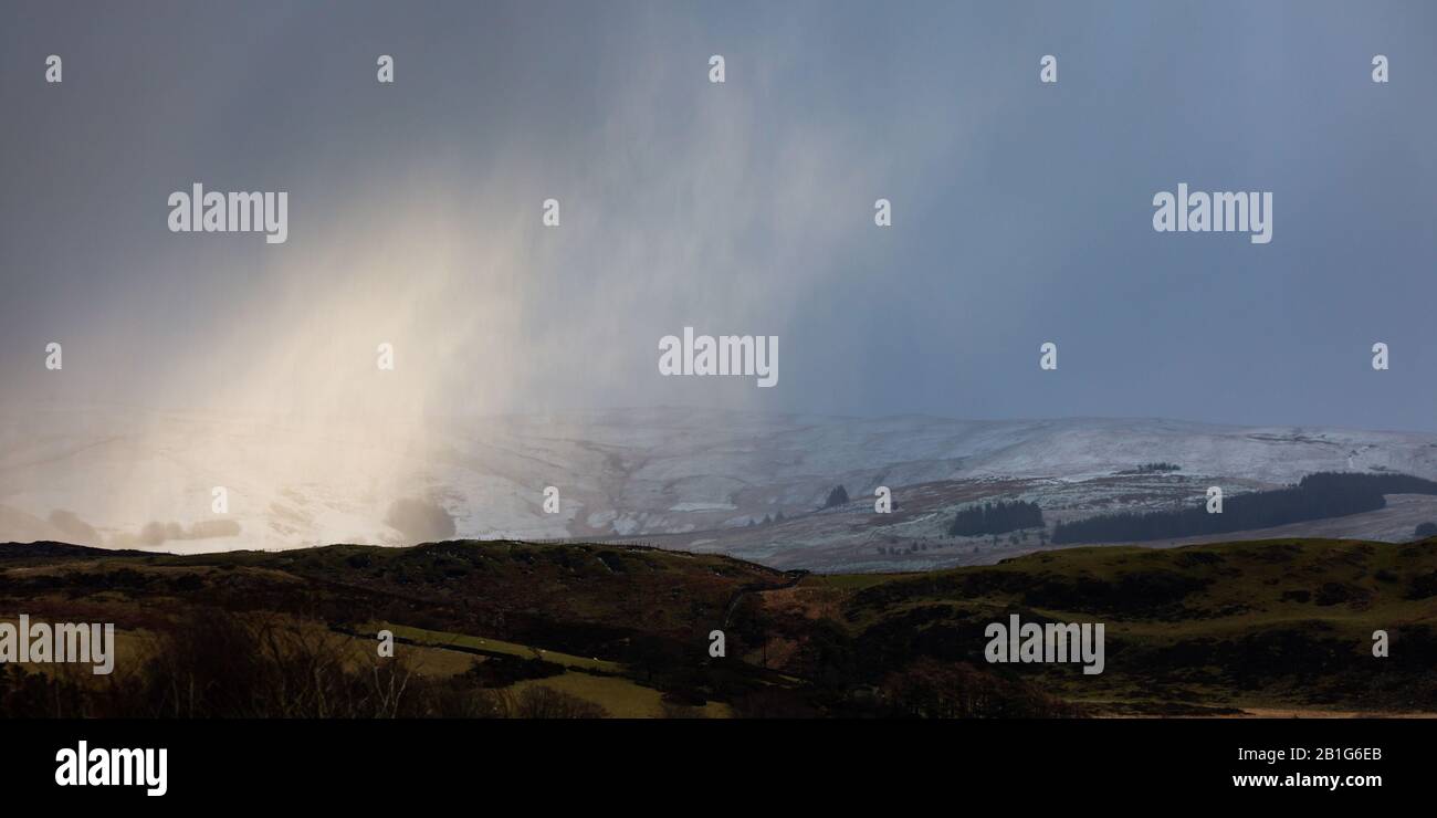 Near Tynygraig, Ceredigion, Wales, UK. 25th February 2020  UK Weather: A cold, breezy afternoon near Tynygraig in Ceredigion, as a small band of light breaks through the cloud, highlighting the snow forming on the Cambrian Mountains in Mid Wales this afternoon. © Ian Jones/Alamy Live News Stock Photo