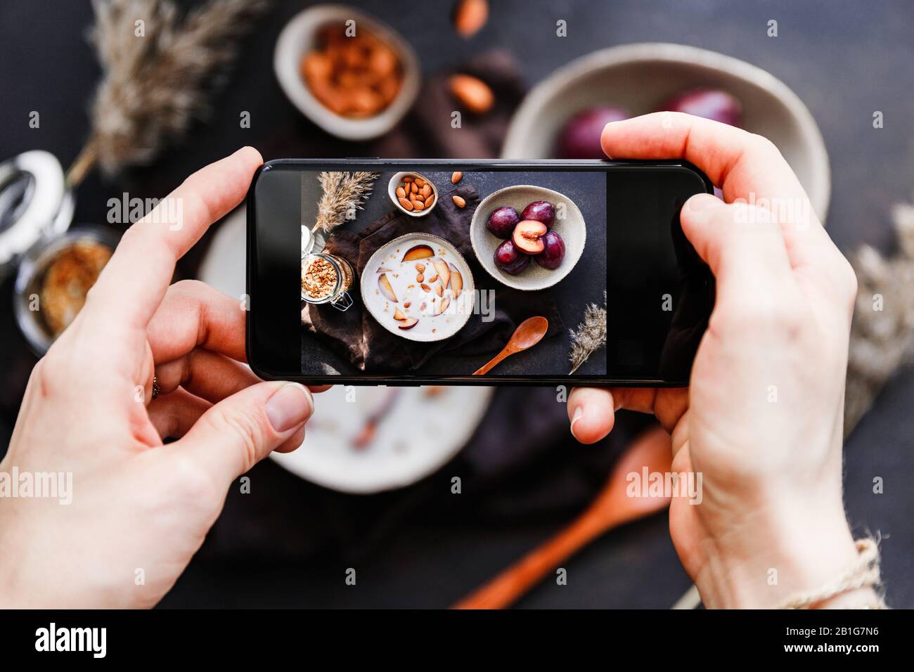 Hands hold smartphone and take picture of morning porridge with almond and sliced plum. Food photography concept. Stock Photo