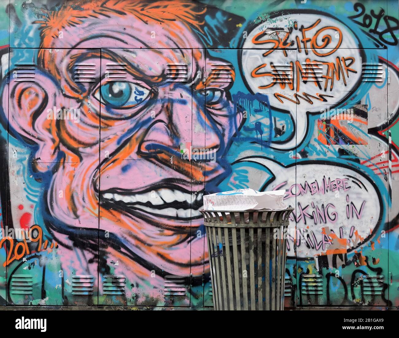 Modern graffiti with a trashcan in front in Porta Garibaldi distrect of Milan, Italy, depicting a big human face speaking Stock Photo