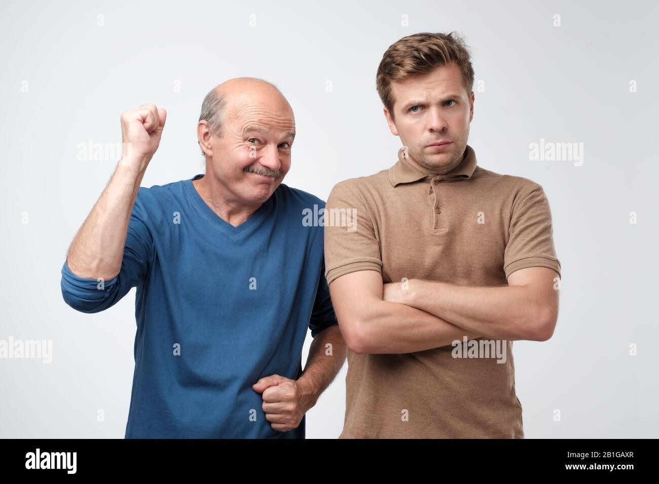 Father feeling glad and son being sad. Family generation quarrel. Studio shot Stock Photo
