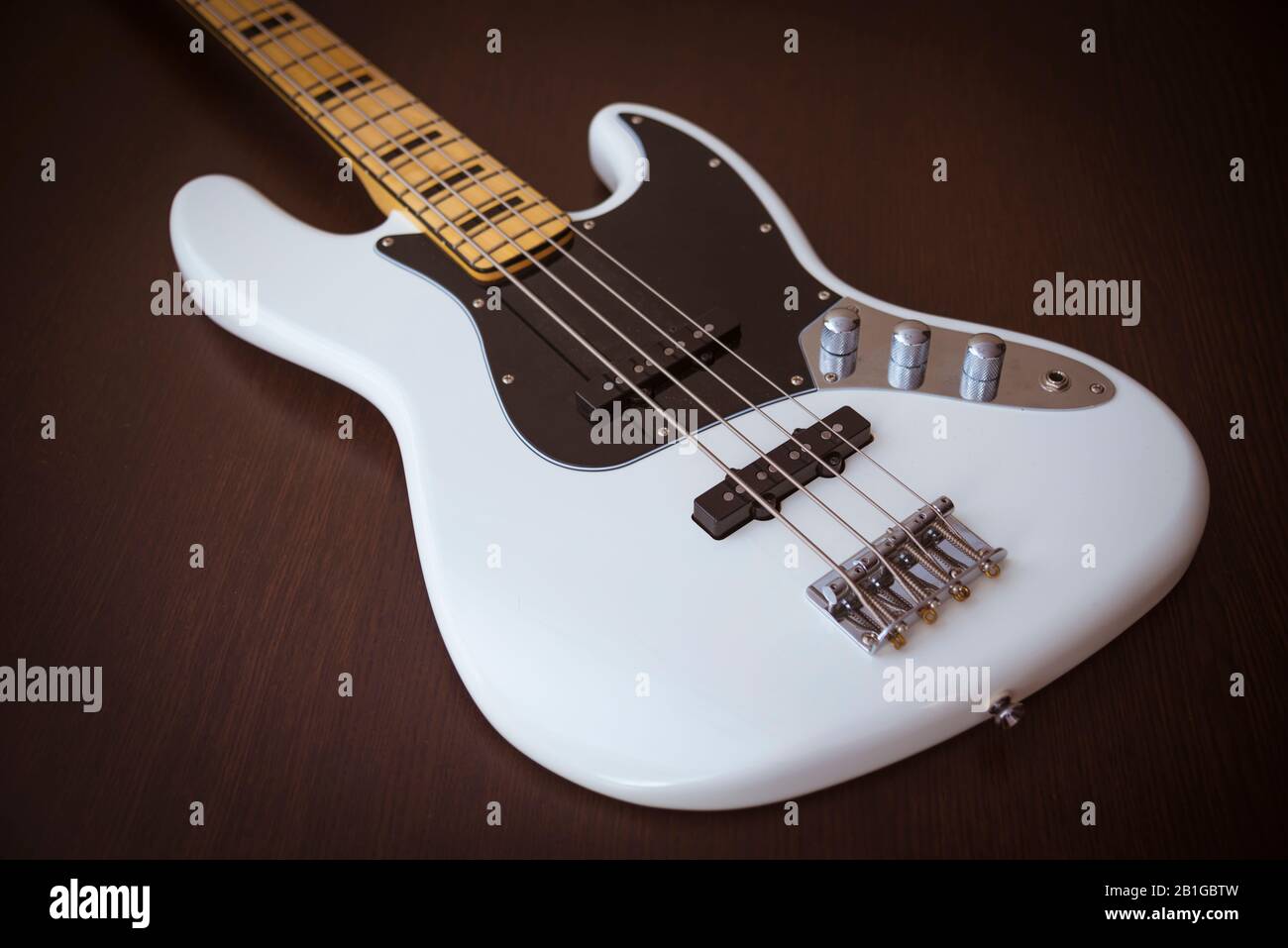 White Electric Bass Guitar with Maple Neck, Black Pickguard, and Black Block Inlays on a Simple Wooden Background Stock Photo