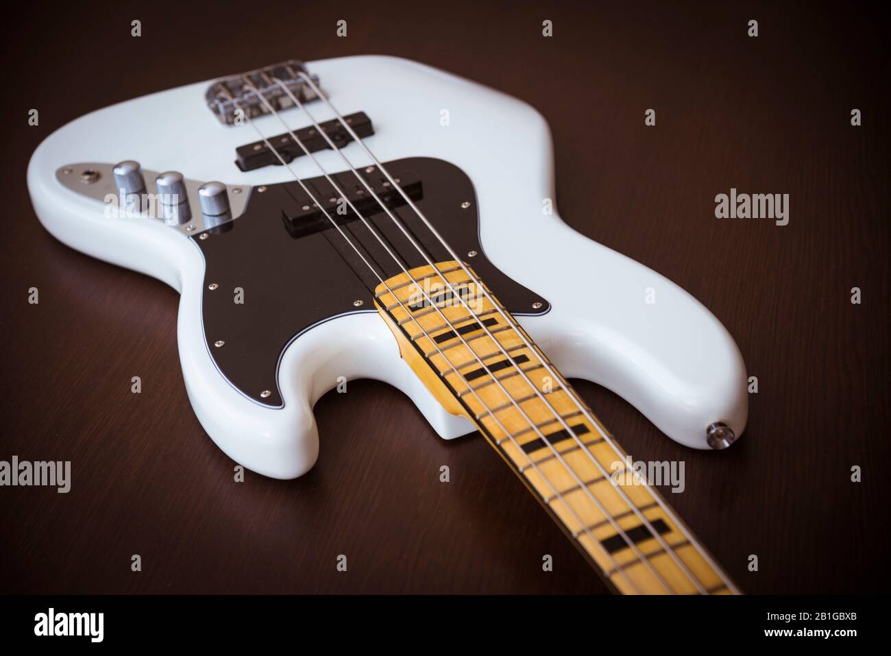 White Electric Bass Guitar with Maple Neck, Black Pickguard, and Black Block Inlays on a Simple Wooden Background Stock Photo