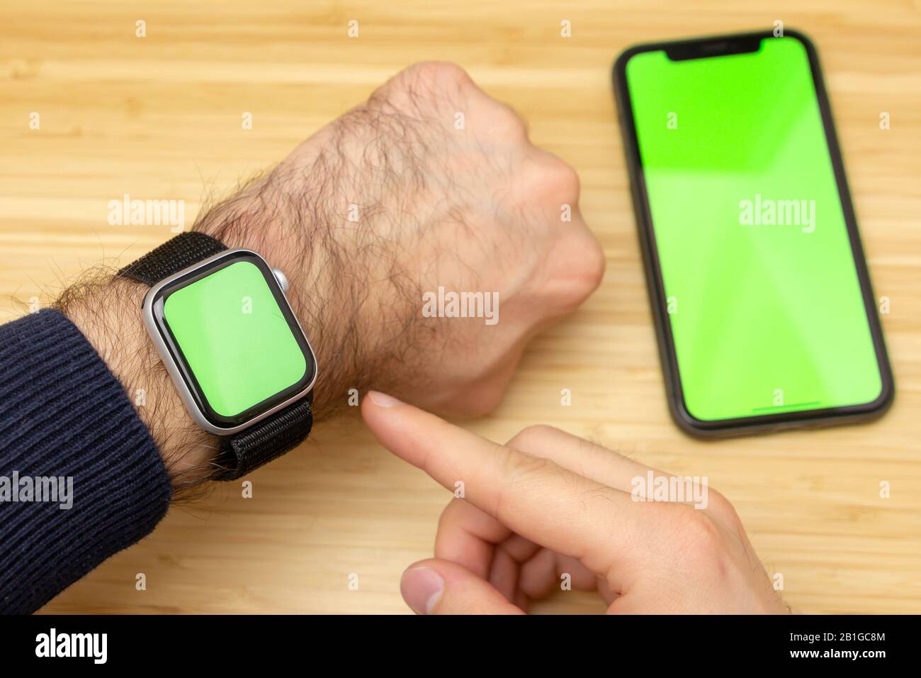 Mockup image of finger touch green screen of smart watch on wrist. Black mobile phone with green screen on the office table on the background. San Stock Photo