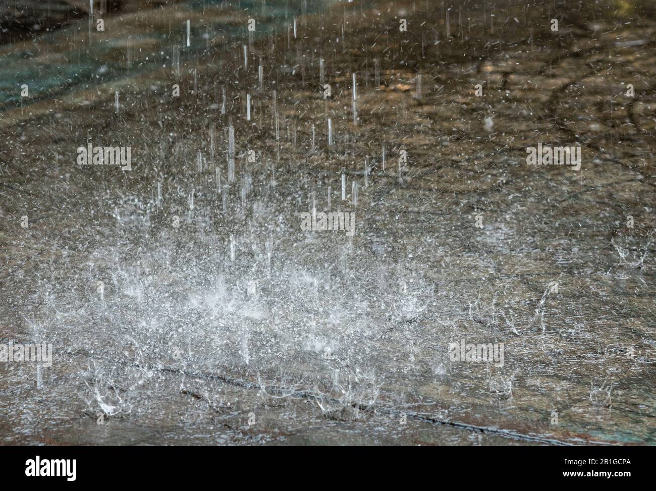 raindrops falling in a torrential downpour on a pavement during heavy weather in the wet winter causing flooding. Stock Photo