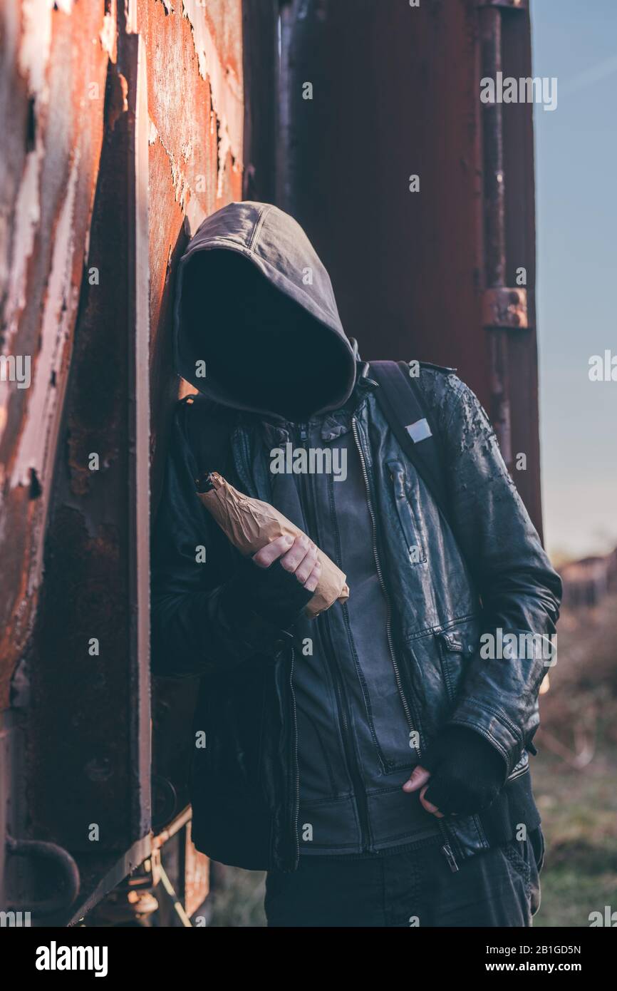 Homeless drunkard drinking alcohol next to old train wagon, drunk man with hoodie in alcoholism concept, selective focus Stock Photo